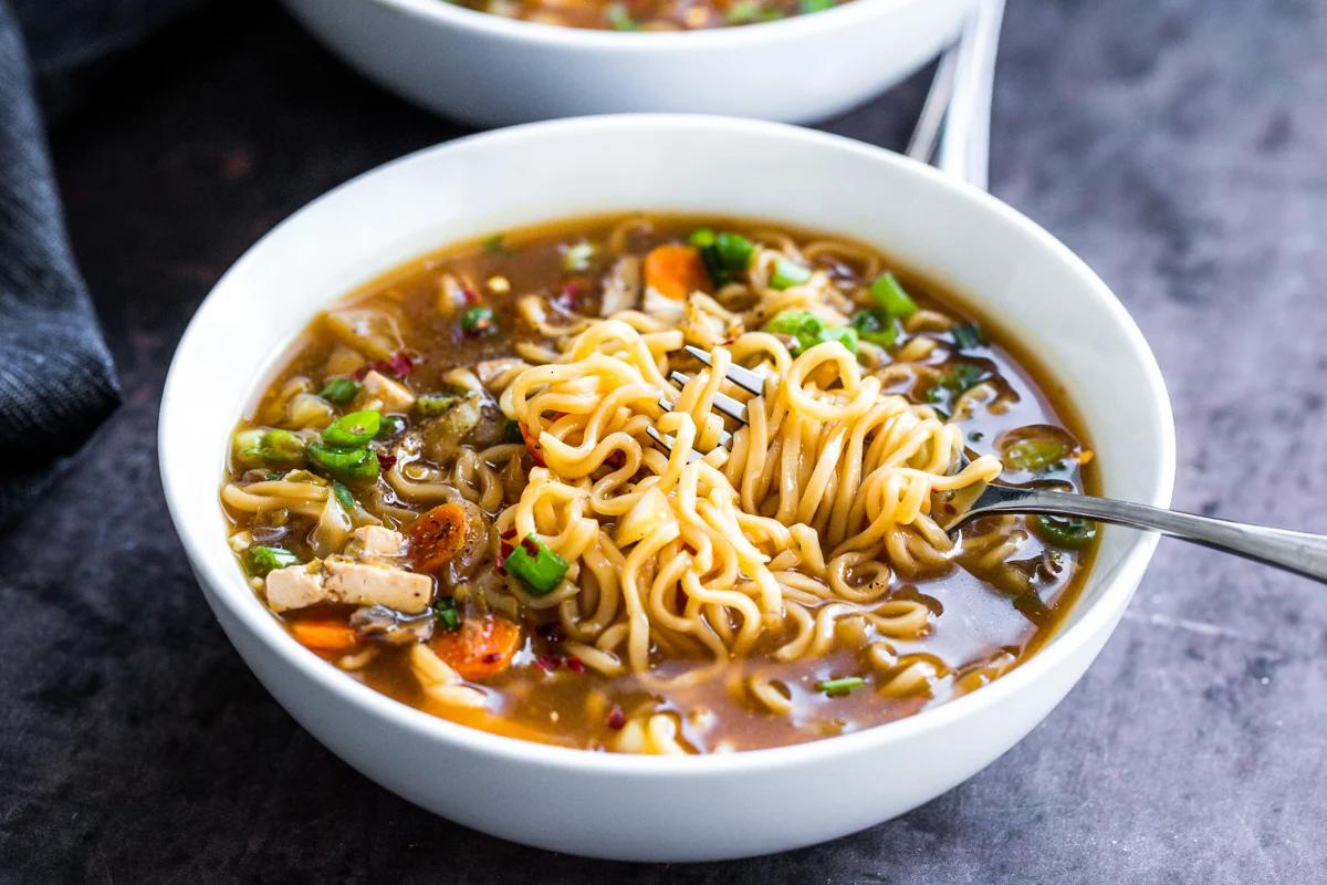 a fork twirling some ramen noodles in a bowl of hot and sour soup