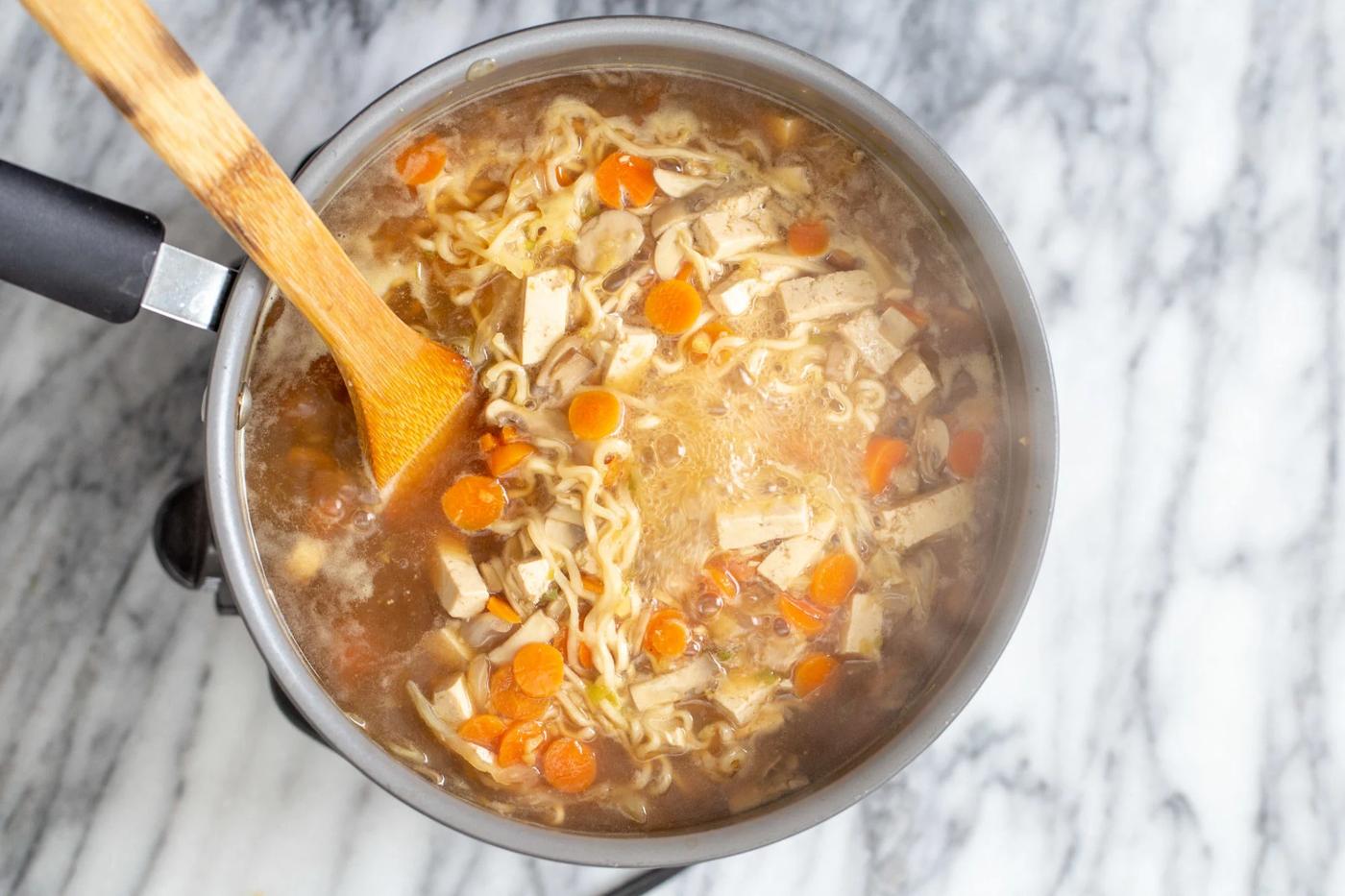a wooden spoon stirring in a pot with vegan hot and sour soup with ramen noodles
