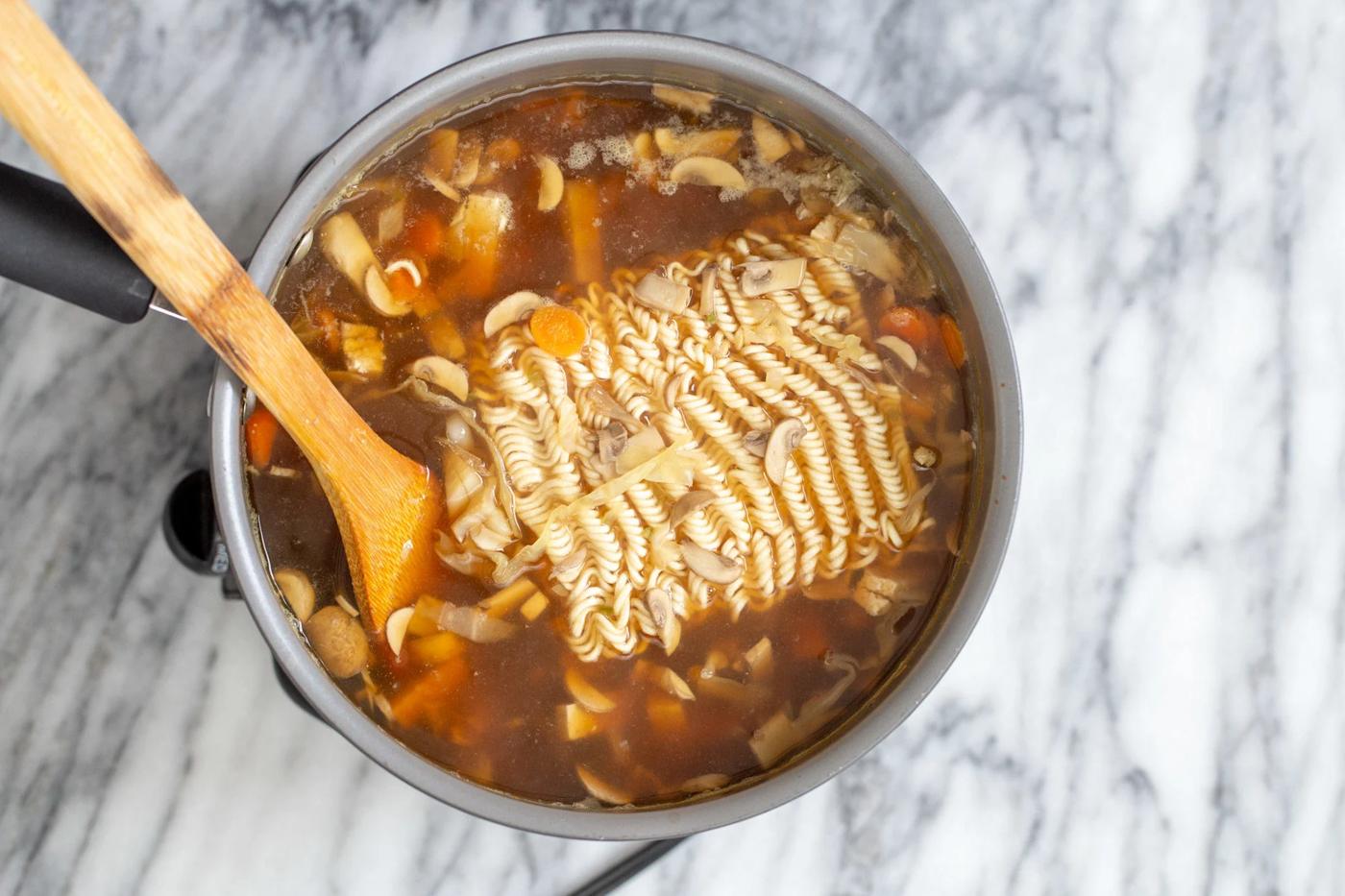 ramen noodles being added to a pot of vegan hot and sour ramen soup