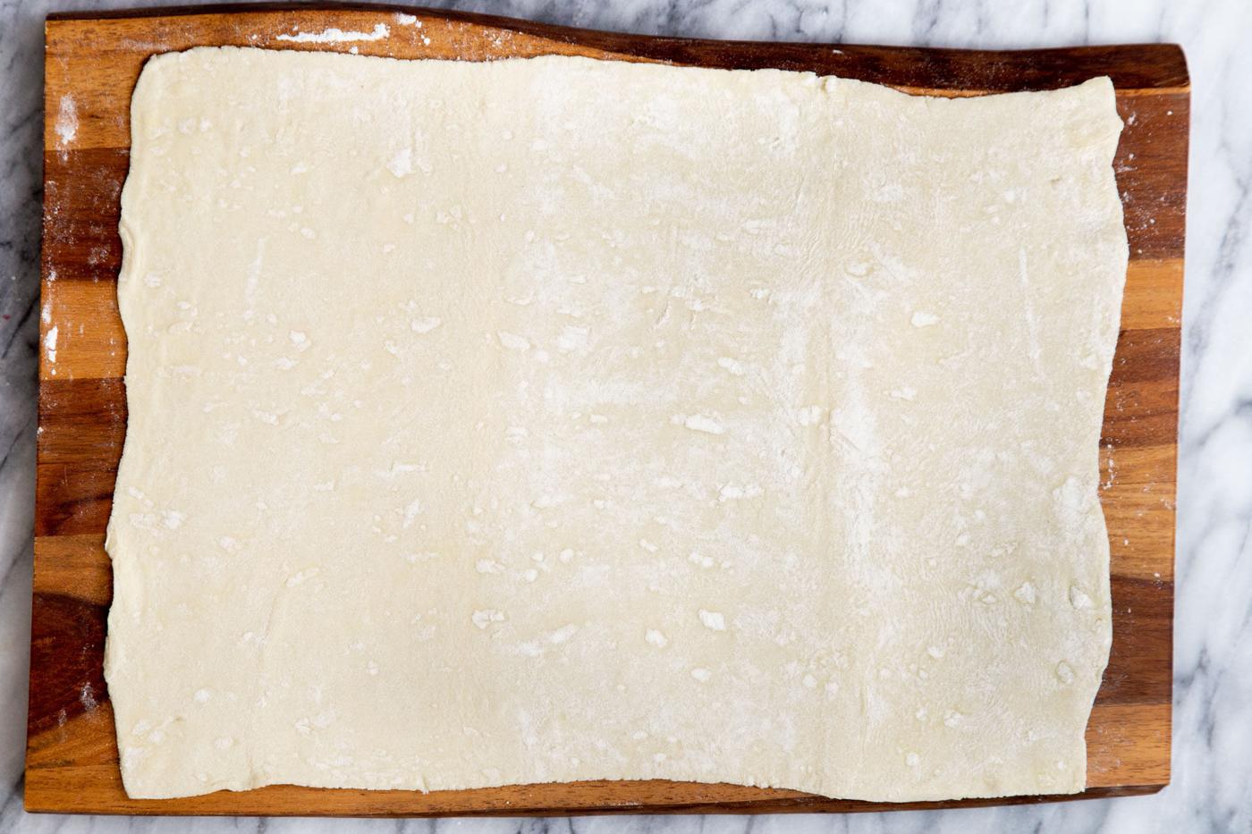 a sheet of puff pastry pasty being rolled out on a chopping board