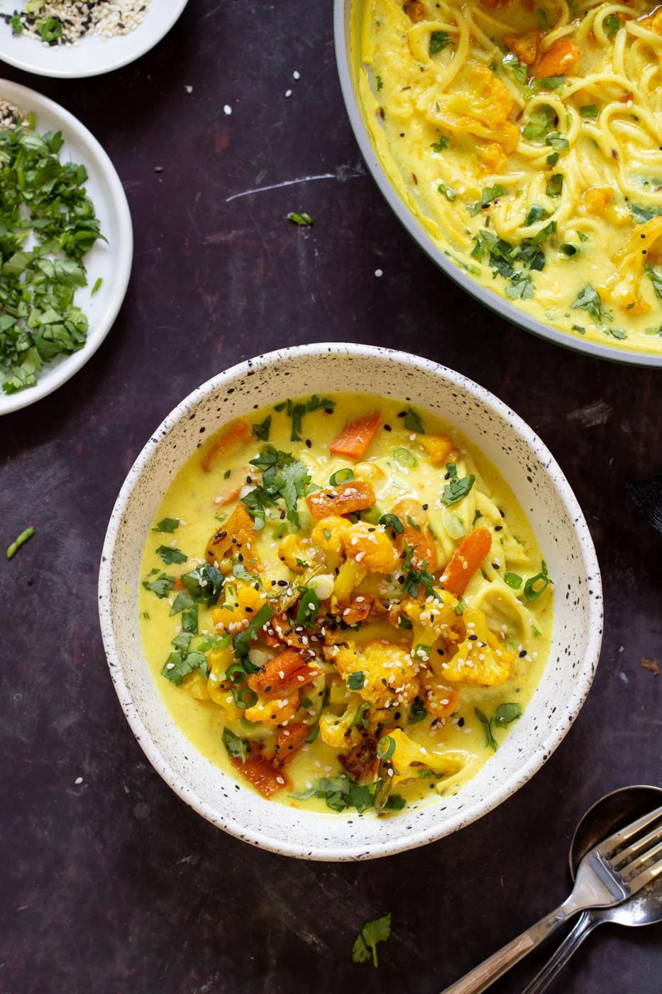 bowl of vegan kadhi pasta with veggies next to the pan and a dish of cilantro