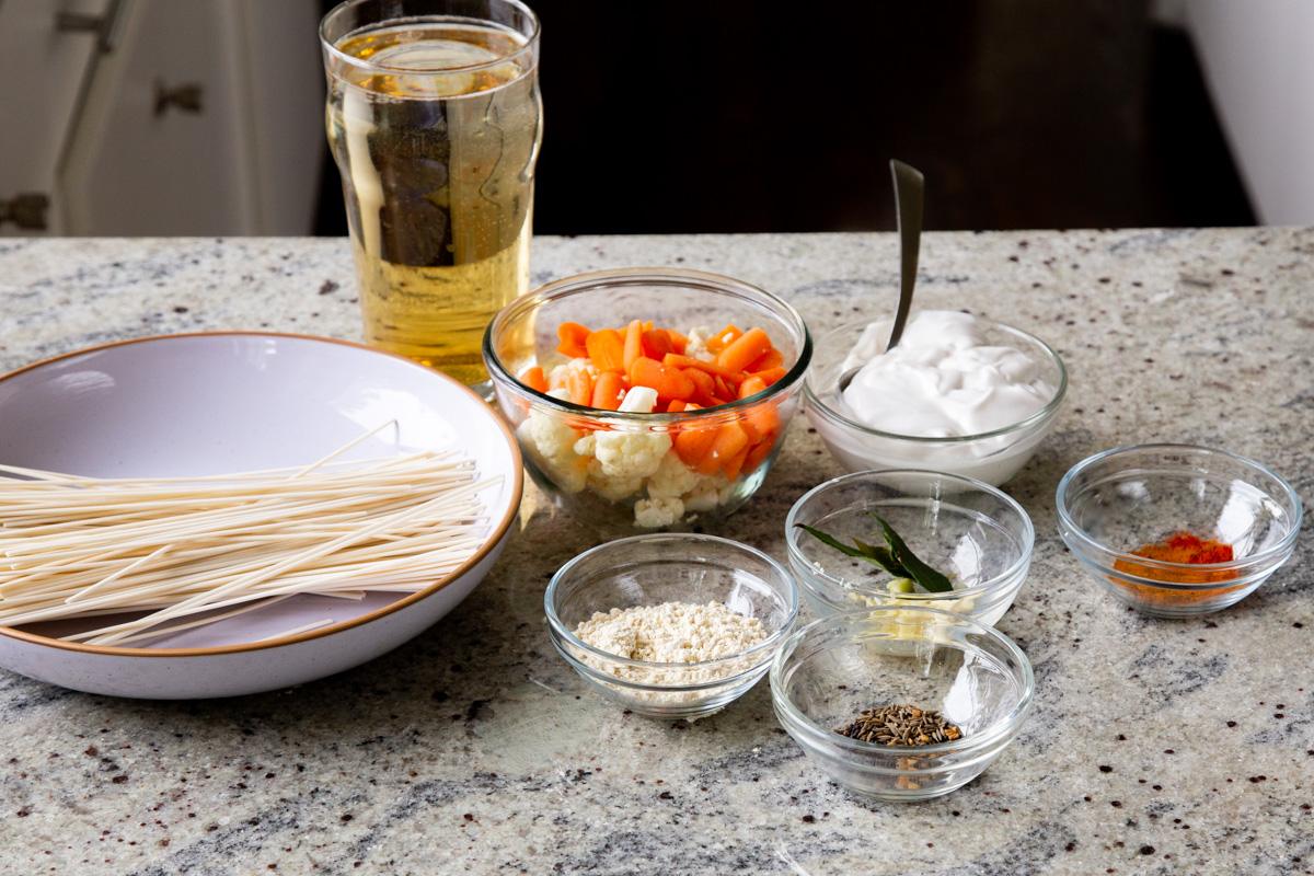noodles, veggies, and vegan kadhi ingredients in bowls on a kitchen counter