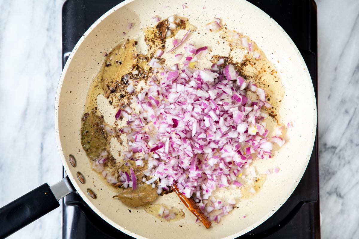 chopped red onion being added to a frying pan tempering