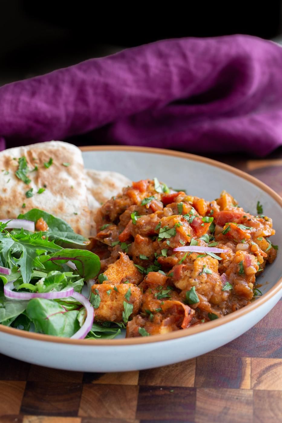 side view of a serving of vegan kadha masala murg curry served with greens and flatbread
