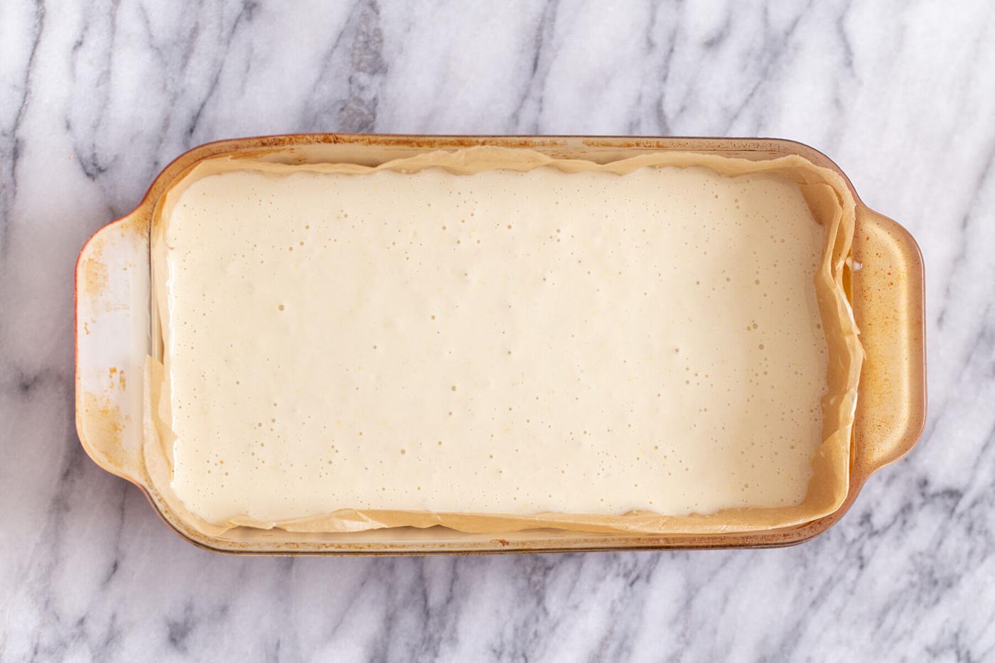 vegan lemon cream filling being poured in a pyrex loaf pan to make lemon bars