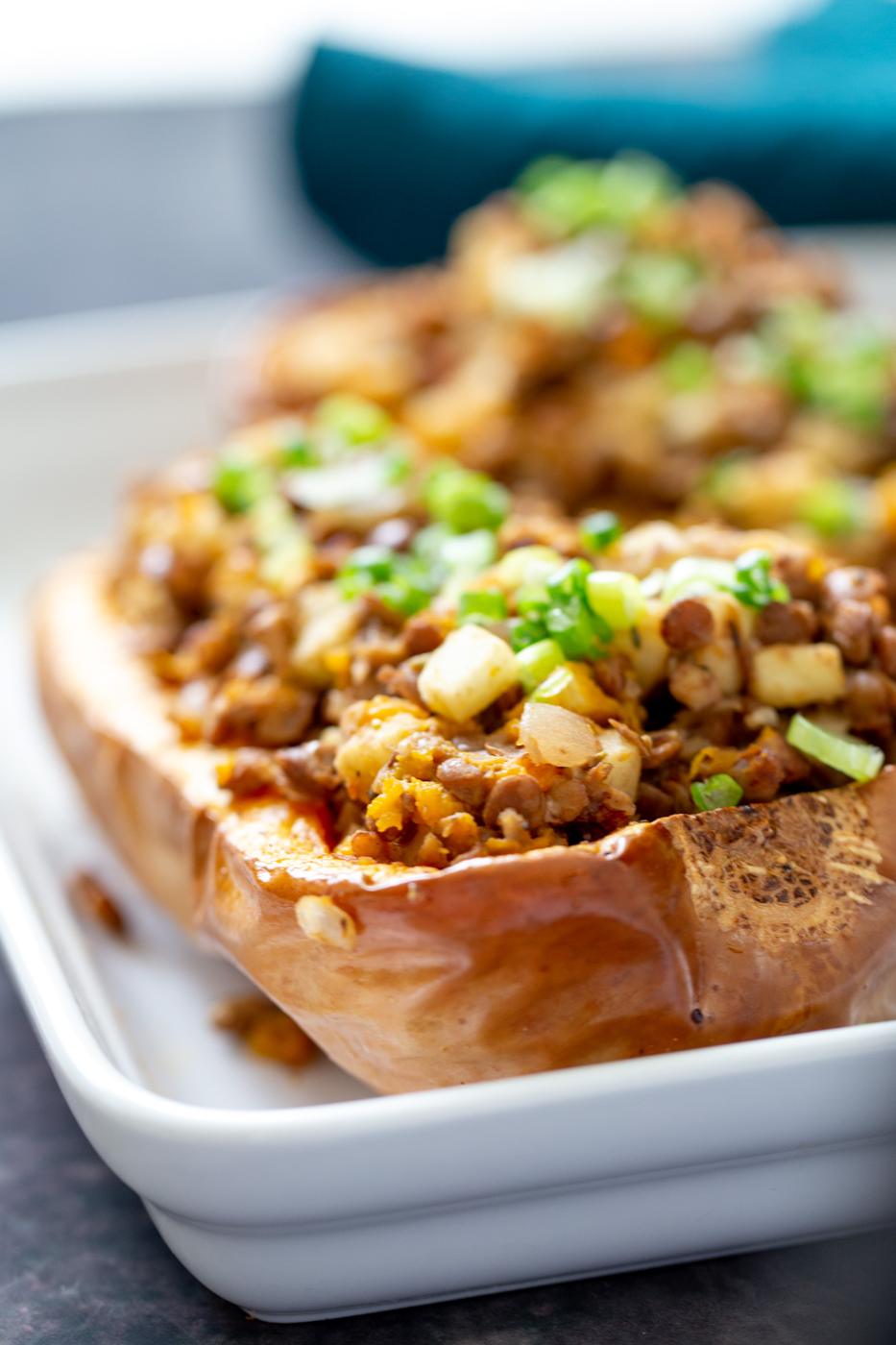 close-up of a lentil and apple stuffed baked butternut squash half in a white casserole dish