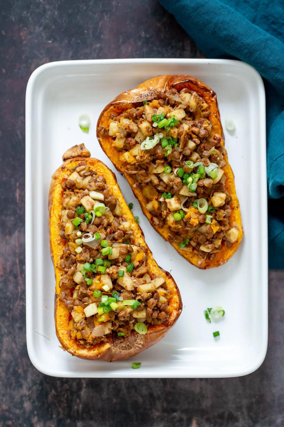 lentil and apple stuffed butternut squash halves in a white casserole dish
