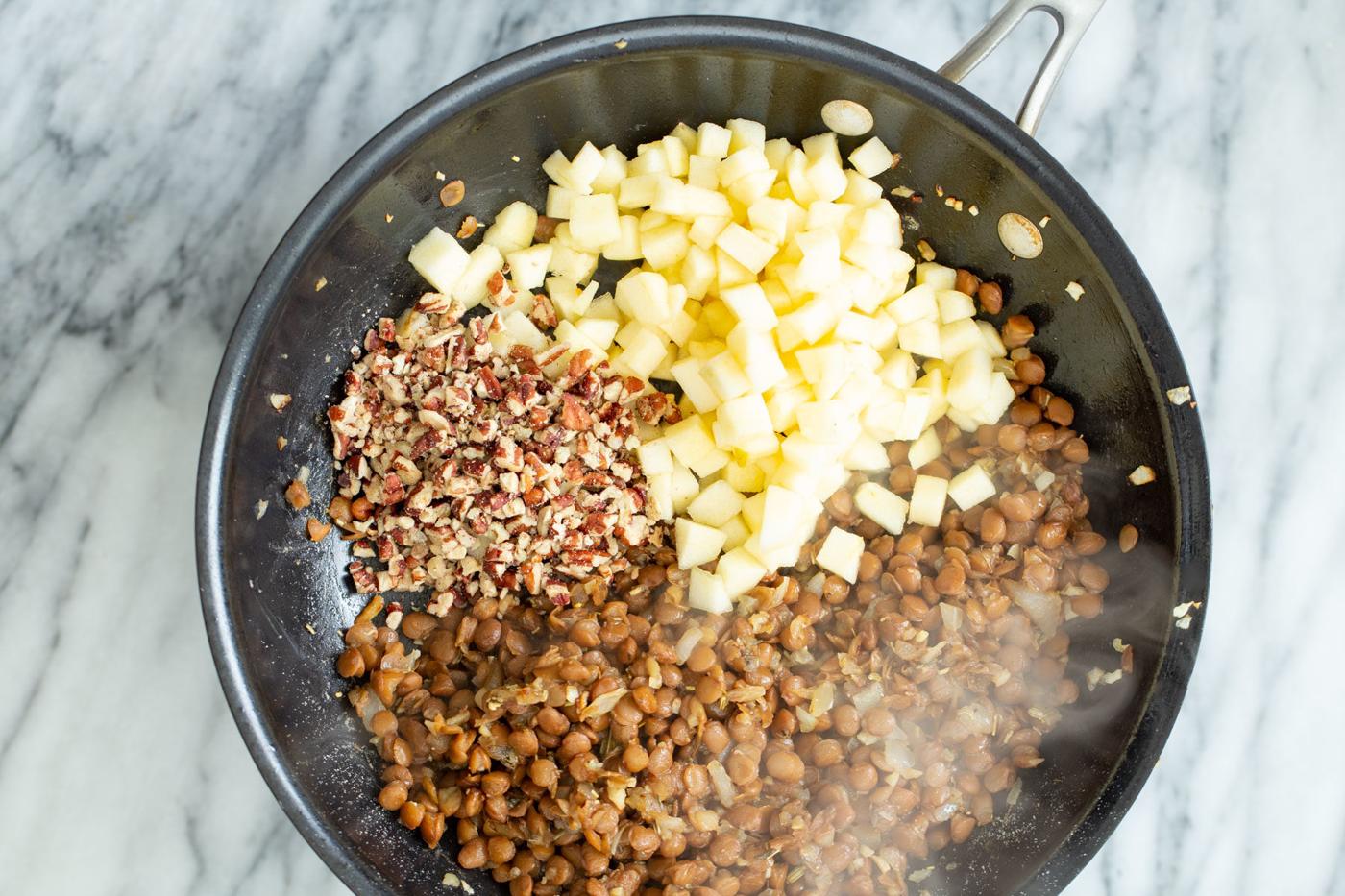 apples and chopped nuts being added to vegan lentil stuffing in a frying pan