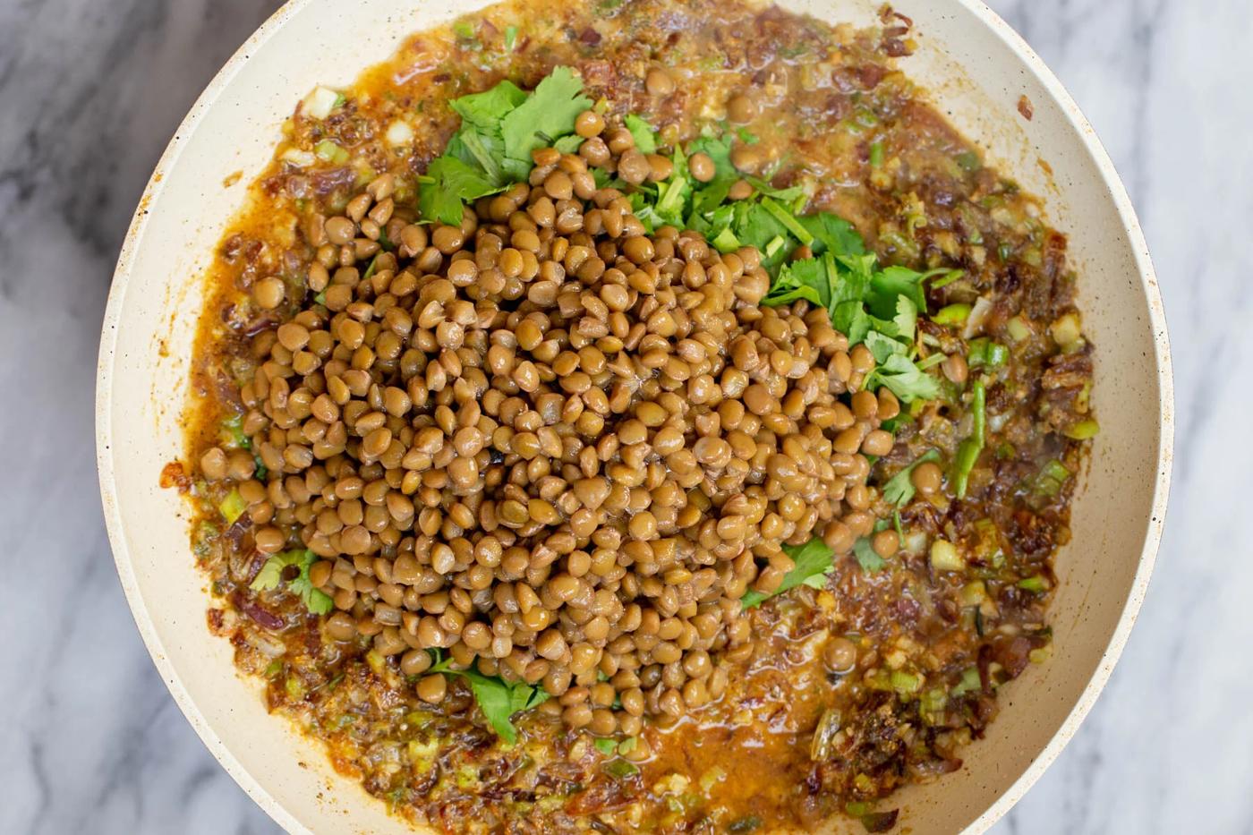 lentils being added to sauteed garlic, ginger and onions to make pie filling