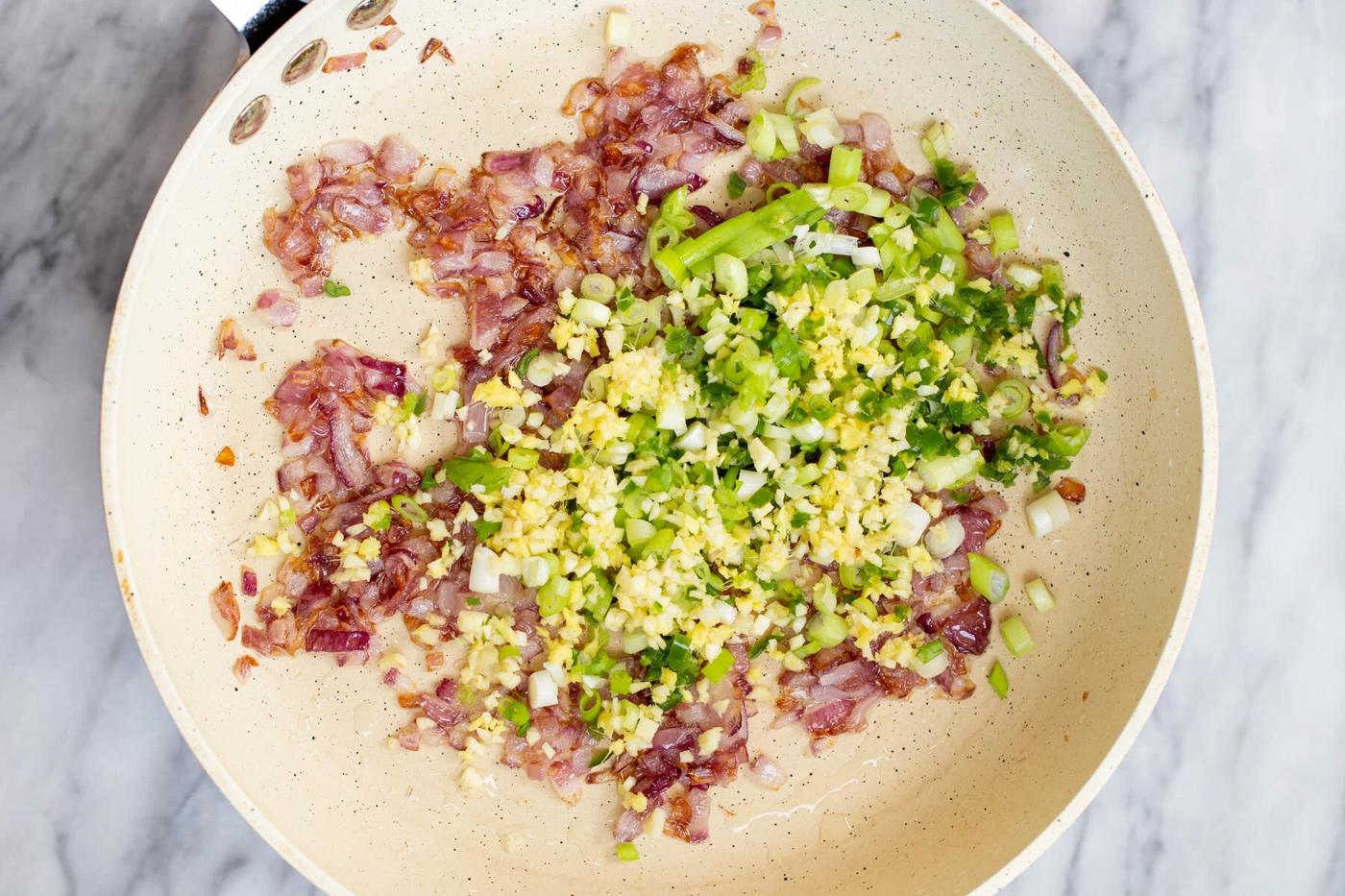 red onion, ginger and green onions being added to a sauteeing pan