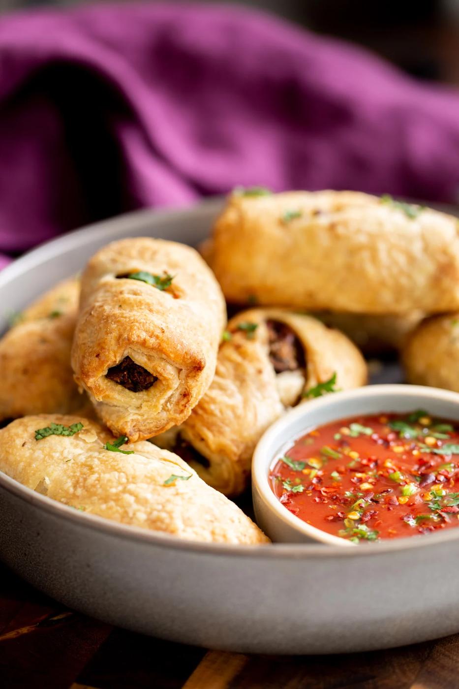 vegan sausage rolls with vegan puff pastry next to a side dish with tomato sauce