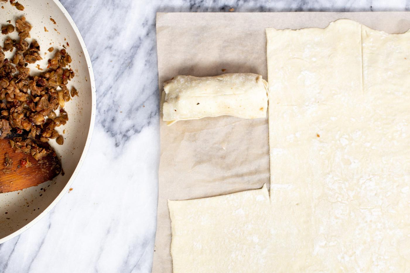 thawed puff pastry being rolled out on a marble countertop