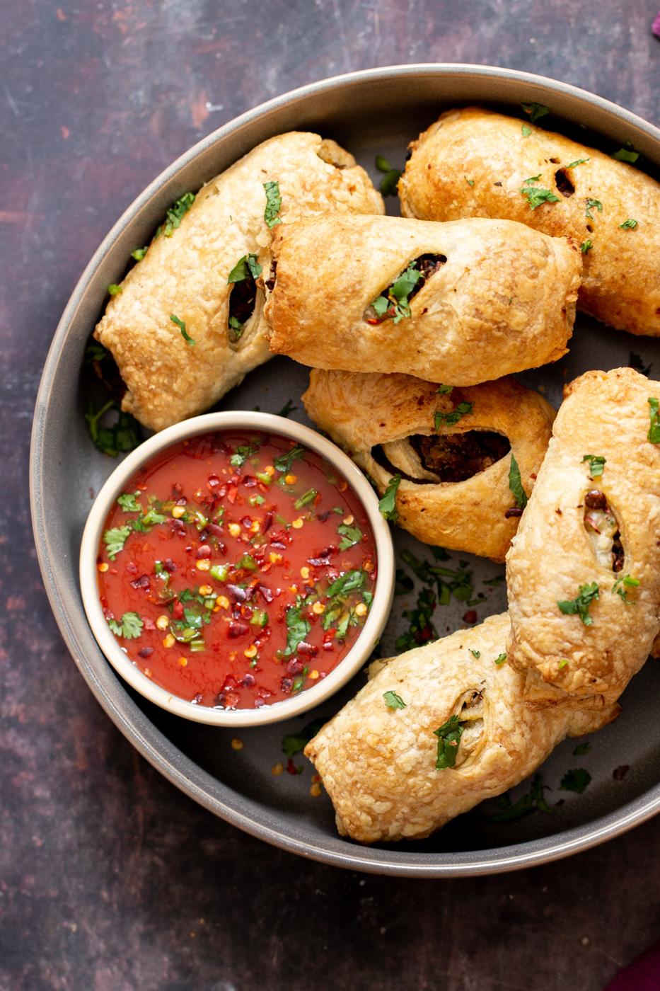 a platter with vegan sausage rolls next to a small dish with tomato sauce