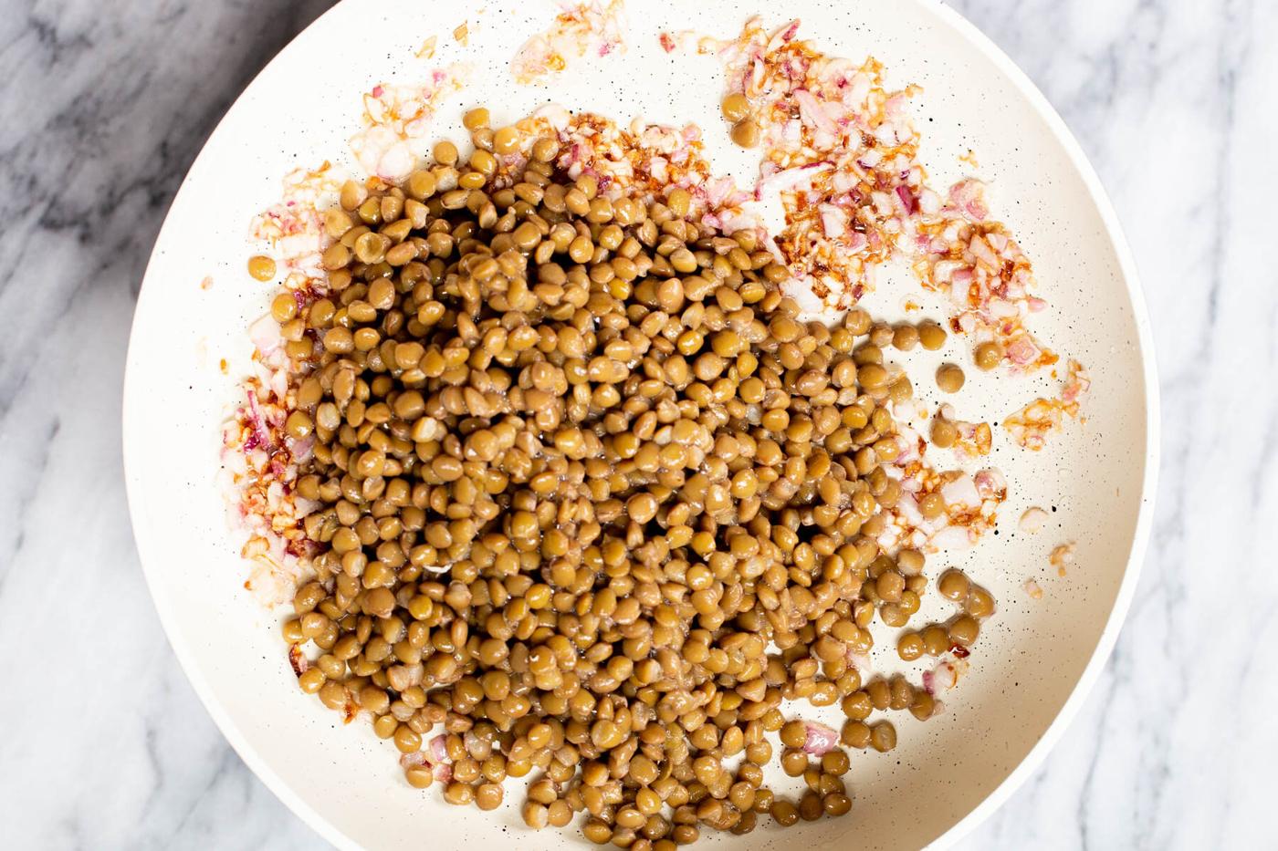brown lentils and diced onions in a white sauteeing pan