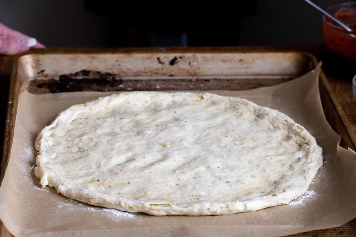 vegan pizza dough being shaped into a circle on a baking sheet