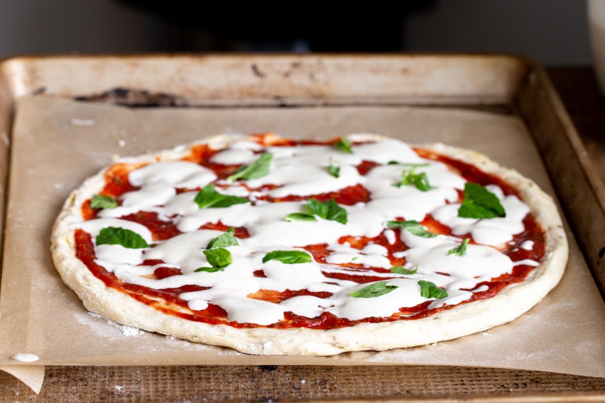 vegan liquid mozzarella cheese being spread over marinara sauce to make pizza