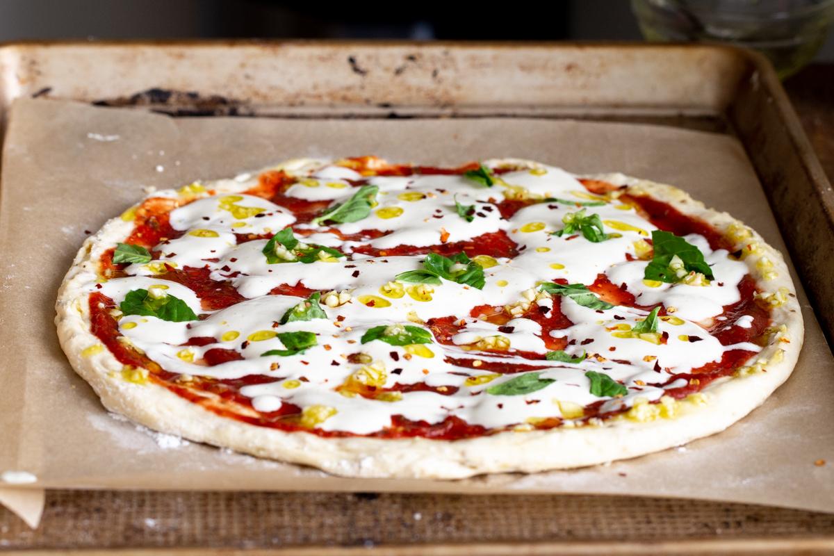 garlic oil and red pepper flaked being sprinkled over vegan mozzarella pizza on a baking sheet