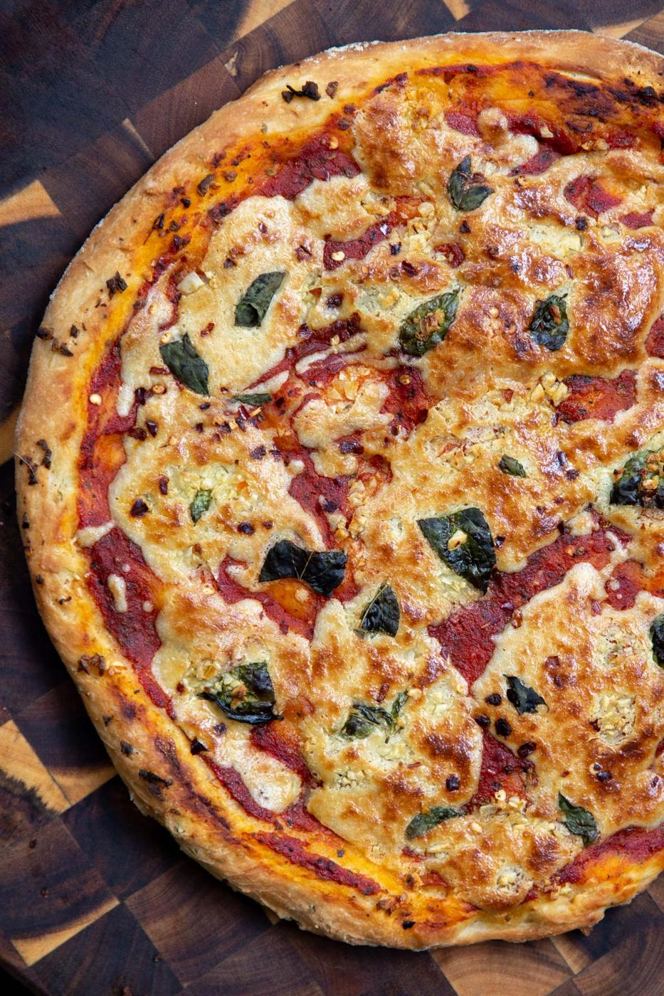 overhead shot of vegan mozzarella pizza with liquid mozzarella and fresh basil on a chopping board