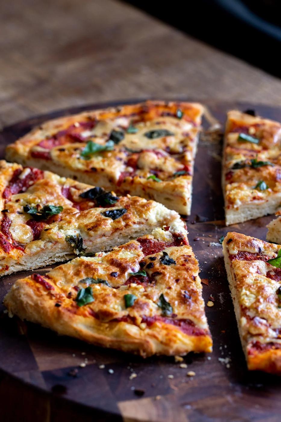 a sliced vegan mozzarella pizza on a wooden chopping board