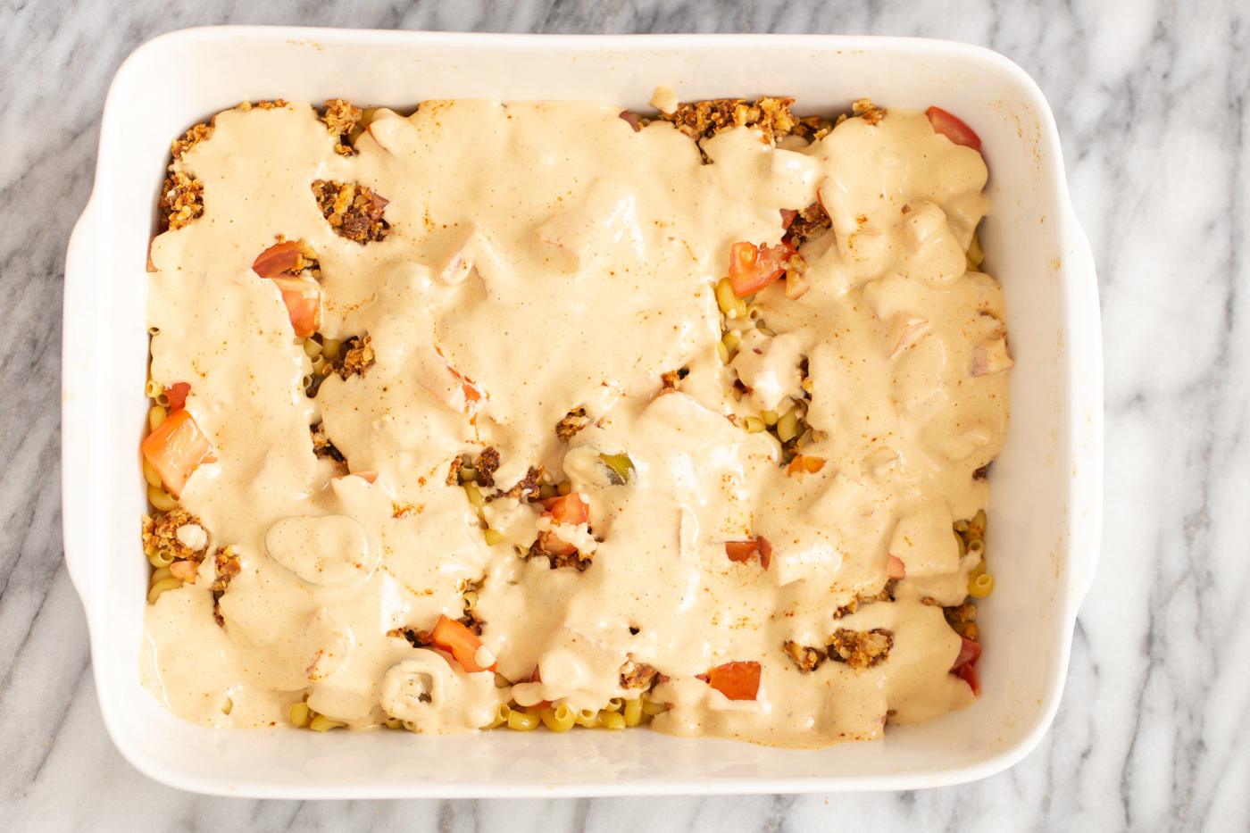 vegan queso sauce being poured over mac and cheese taco casserole