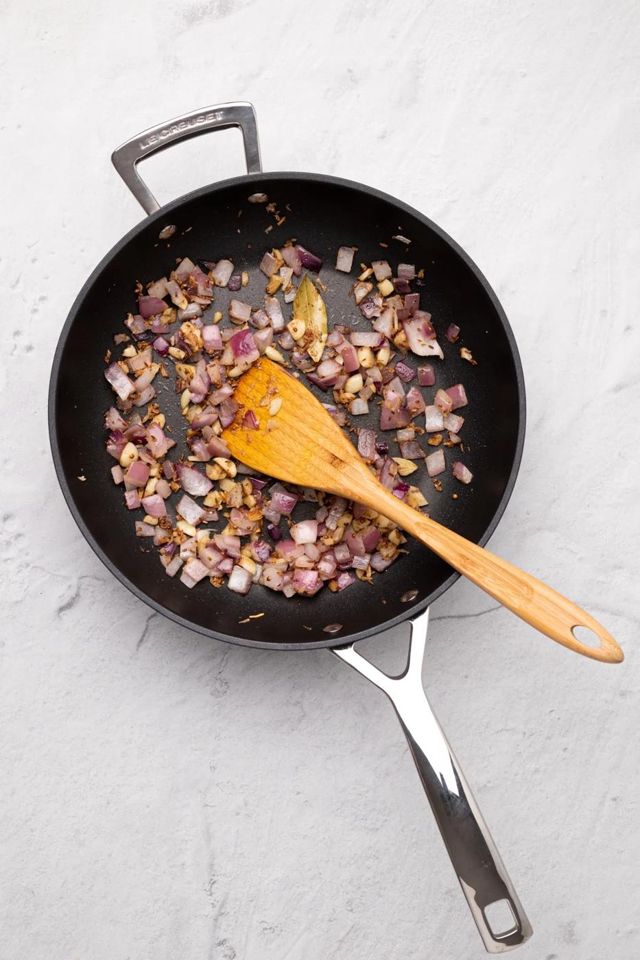onions being stir-fried in a black skillet with spices to make malai kofta gravy