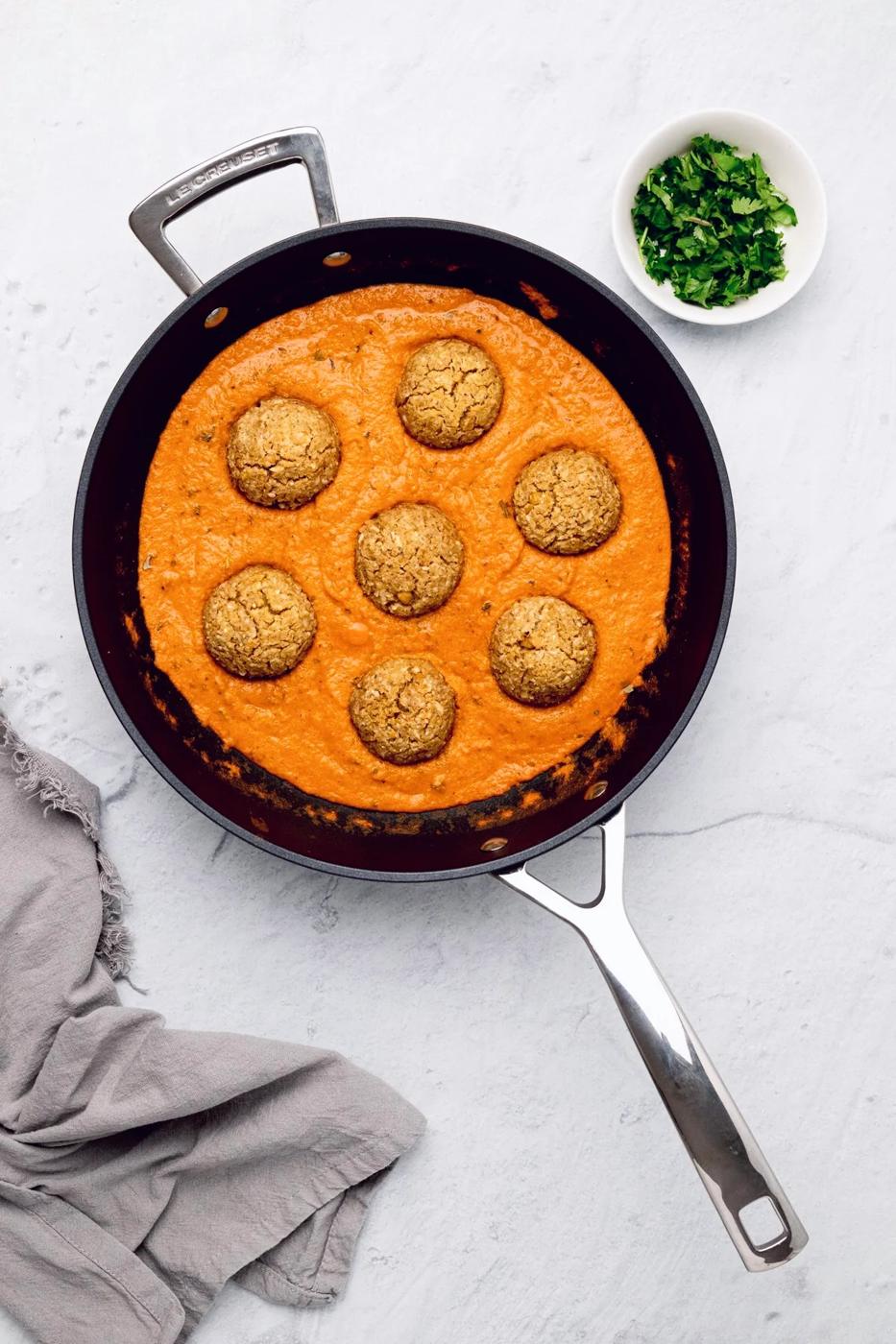 overhead shot of a skillet with vegan kofta in a dairy-free Indian gravy with chopped cilantro on the side