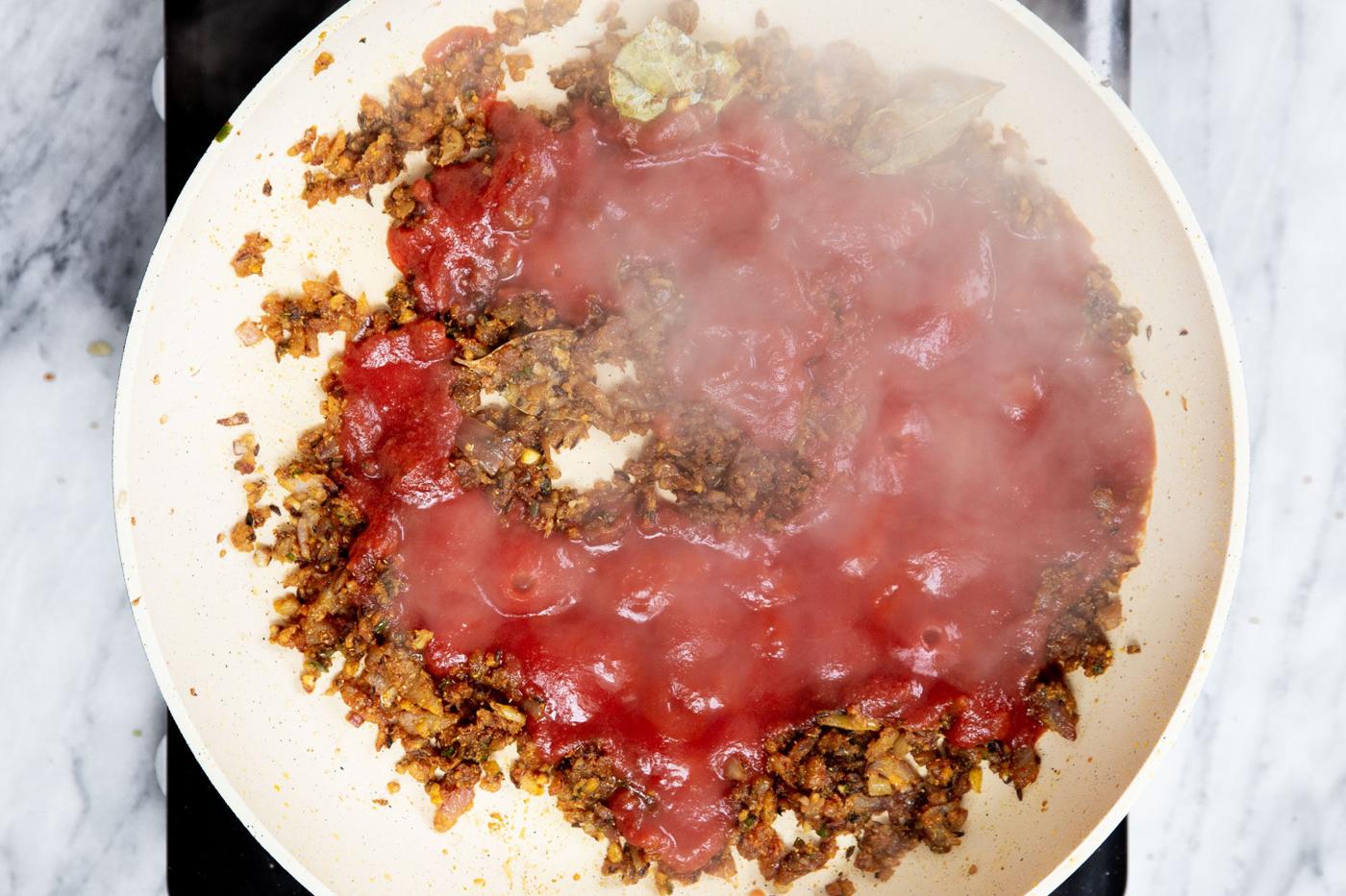 tomato paste being added to a sauteein pan with onion and spices