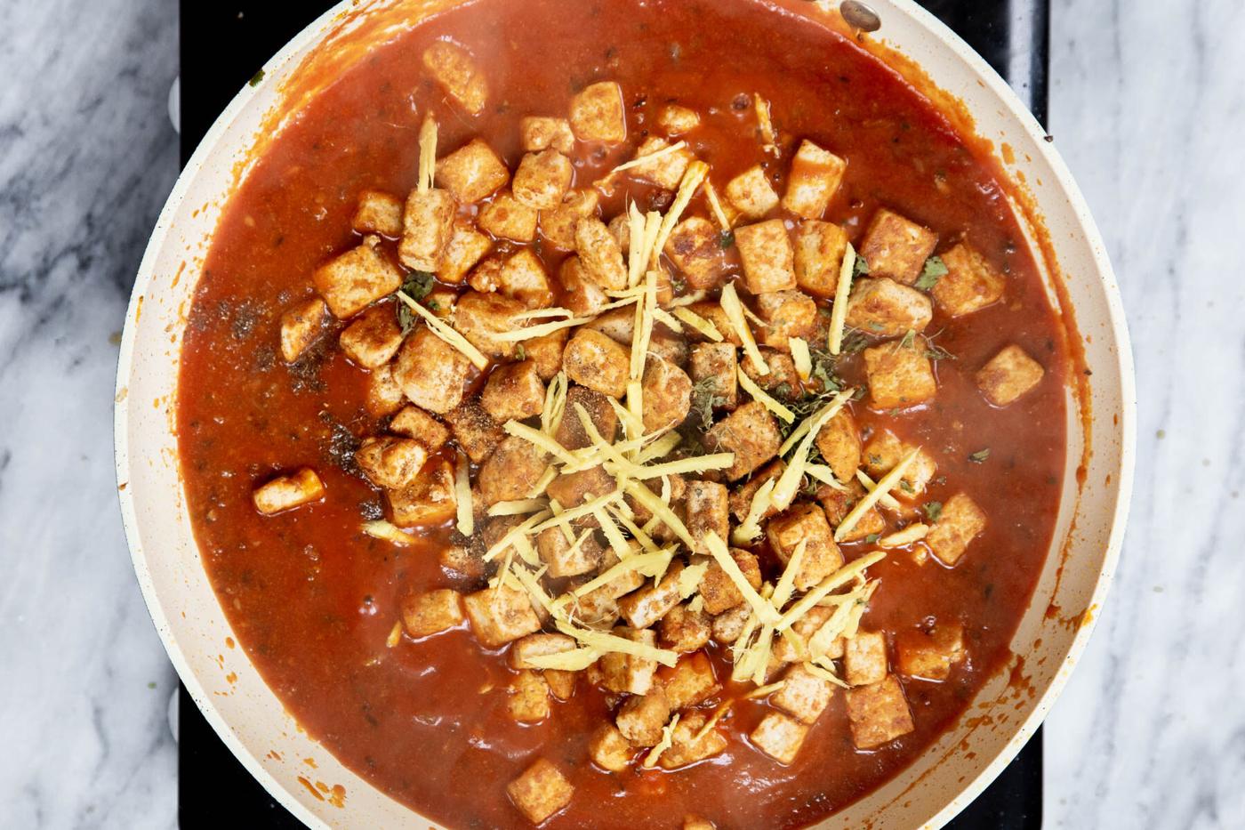baked tofu being added to a sauteeing pan with spiced tomato sauce
