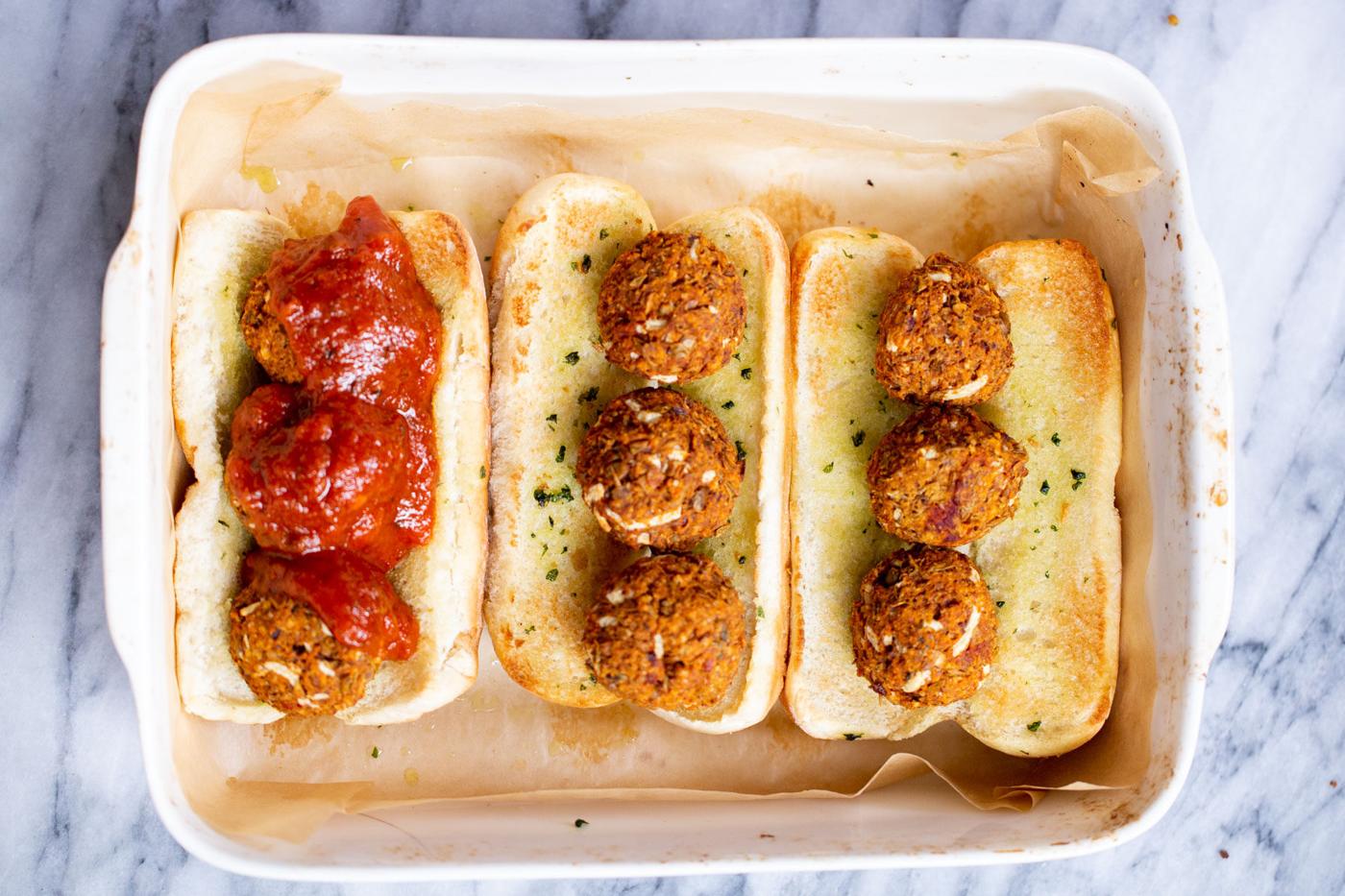 a casserole dish with vegan meatball subs topped with lentil meatballs and marinara sauce