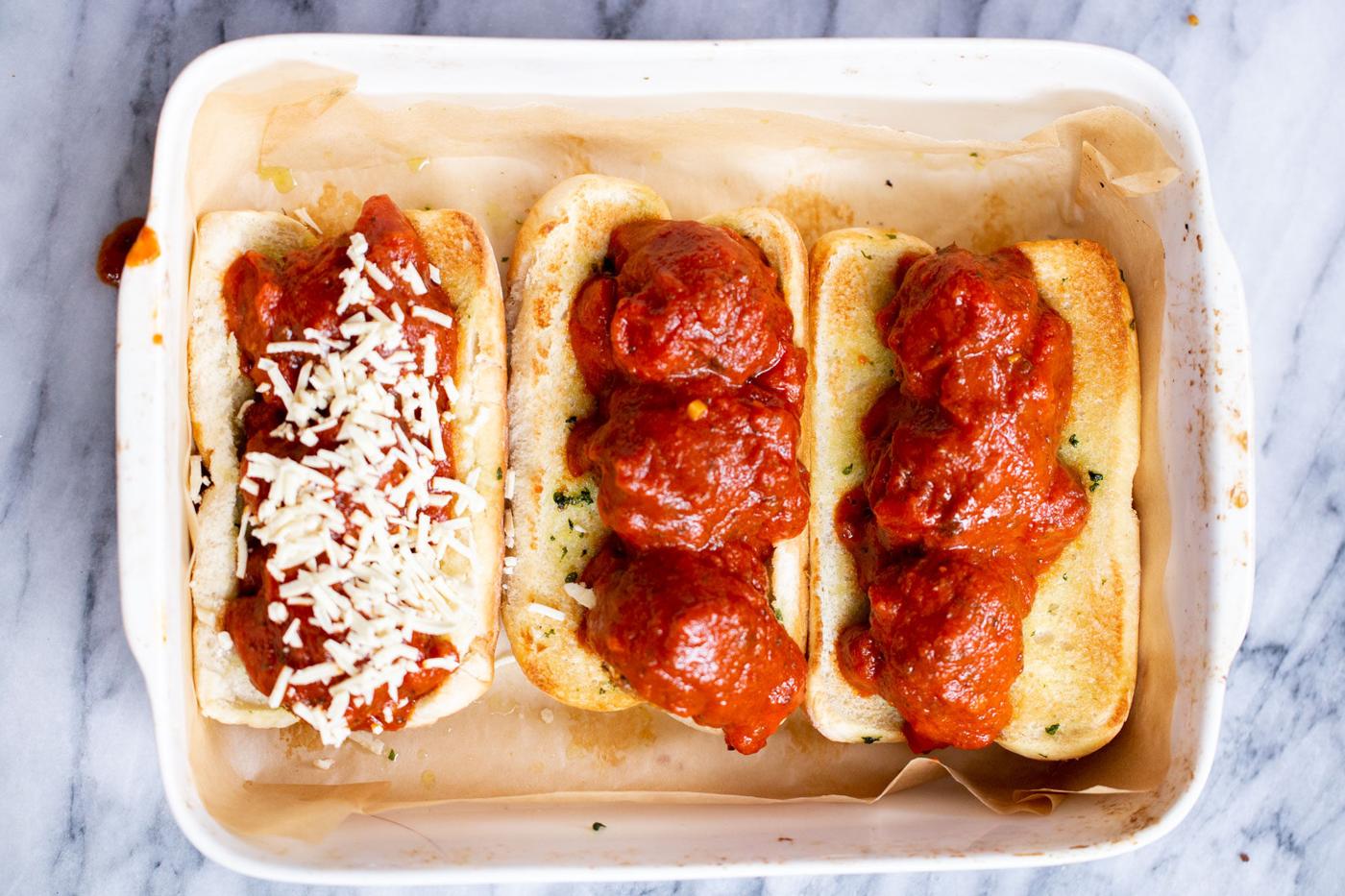 vegan meatball subs topped with lentil meatballs being assembled with marinara sauce and shredded cheese