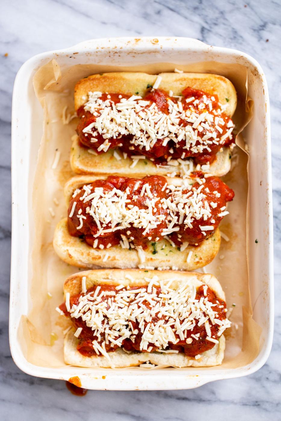a casserole dish with vegan meatball subs topped with shredded cheese