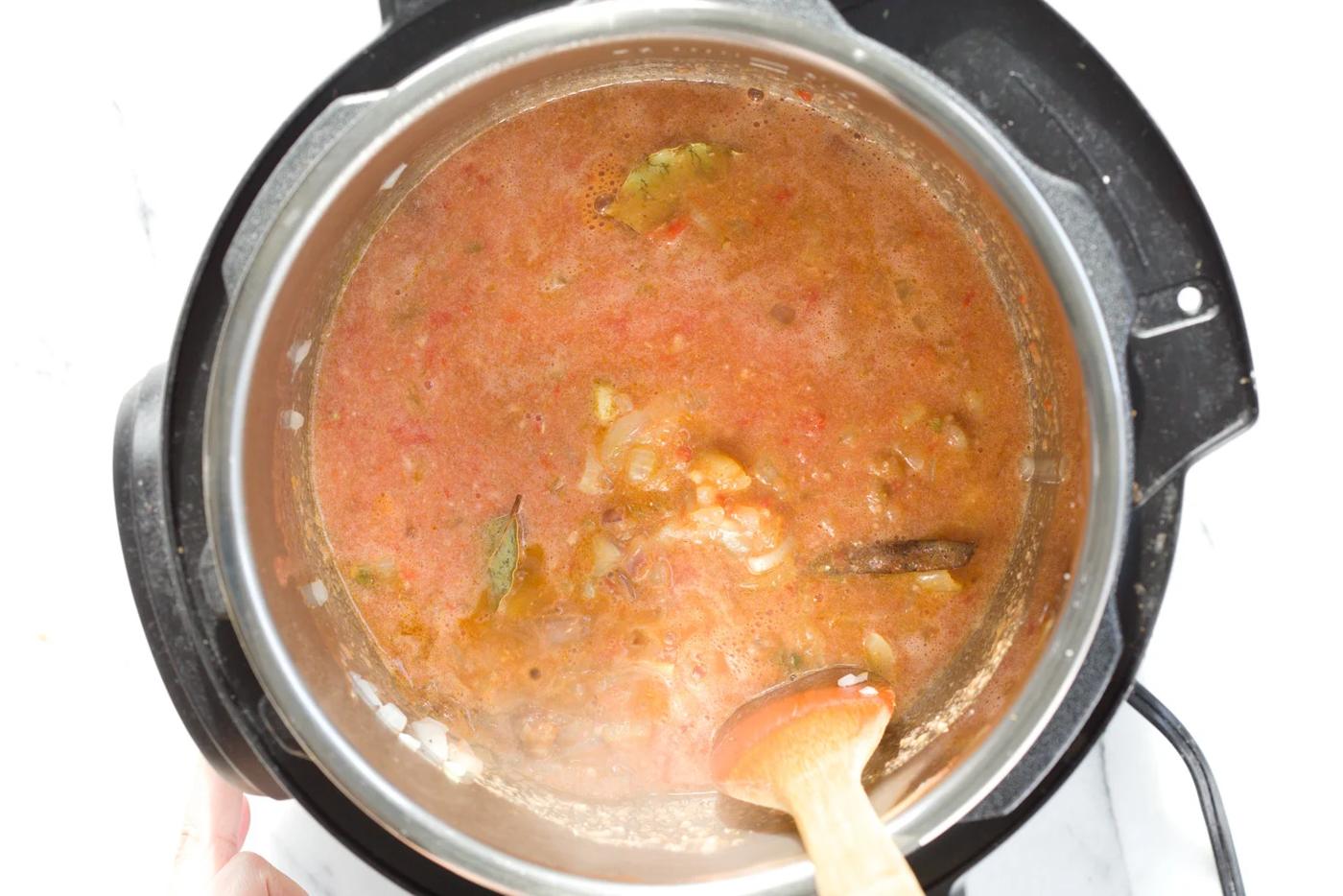 onions, garlic, tomato paste and spices being stirred in an Instant pot to make Vegan curry recipe