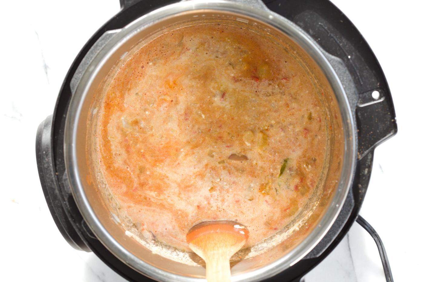 dairy-free milk being stirred into a vegan fenugreek chicken curry made with soy curls