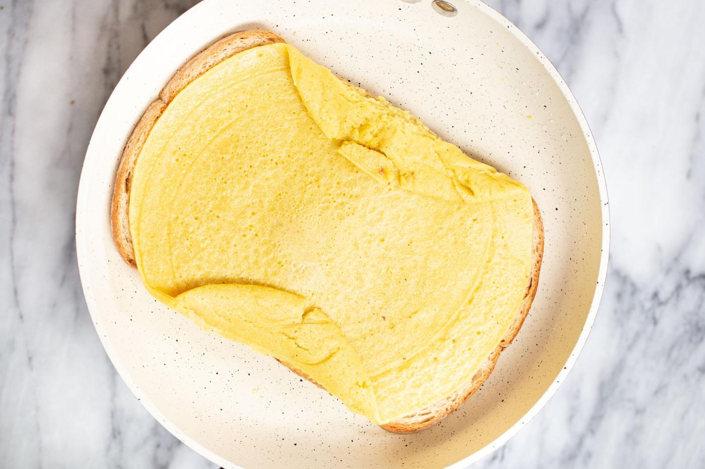 process shot of vegan fold over tiktok egg sandwich being made in a white sauteeing pan