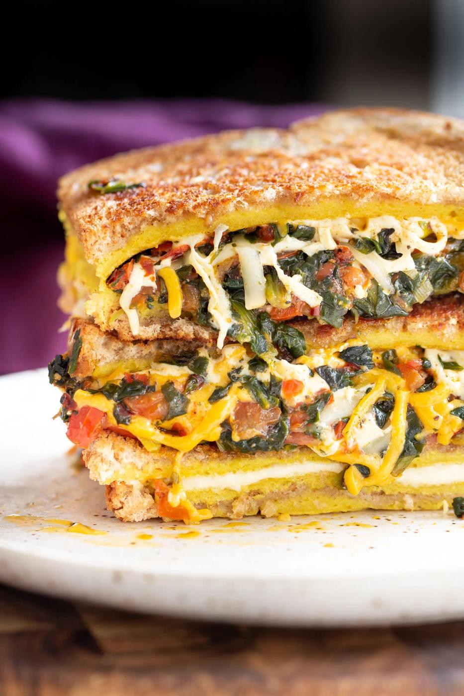 filled spinach and cheese vegan egg sandwiches stacked on a plate