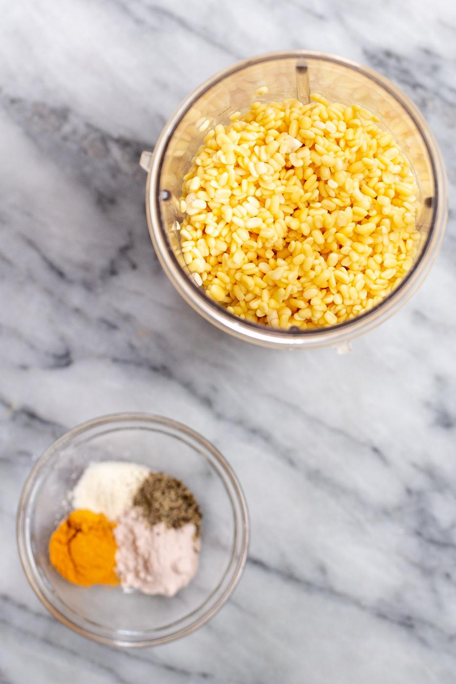 moong dal in a blender with a small dish with spices on the side