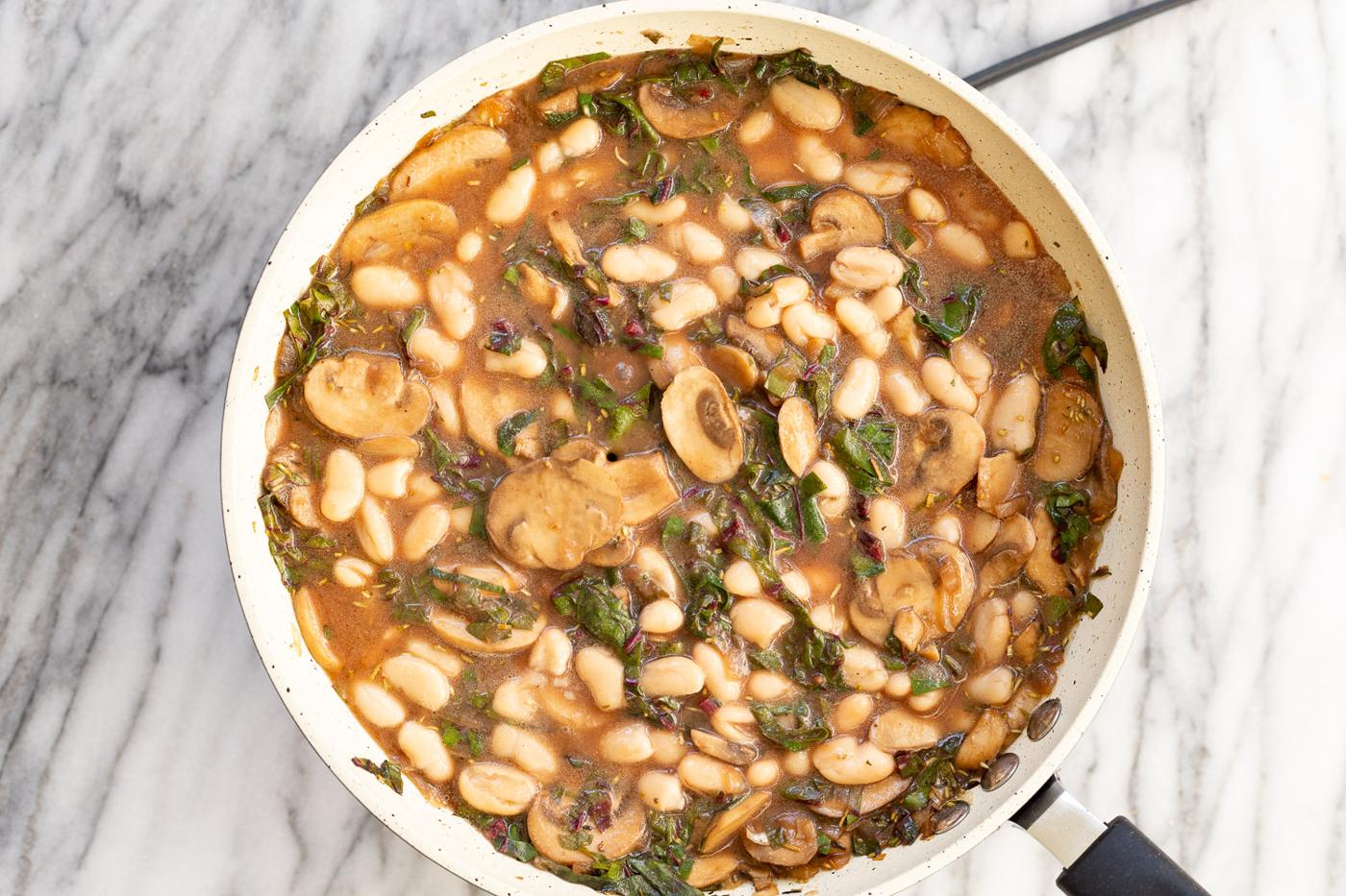 Cannellini beans added to a white skillet