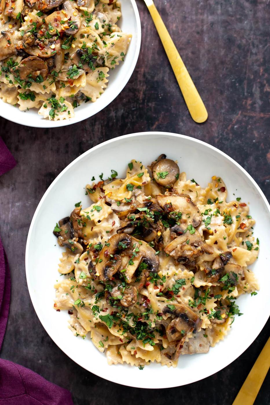 overhead shot of two plates of vegan mushroom stroganoff served on farfalle topped with chopped parsley