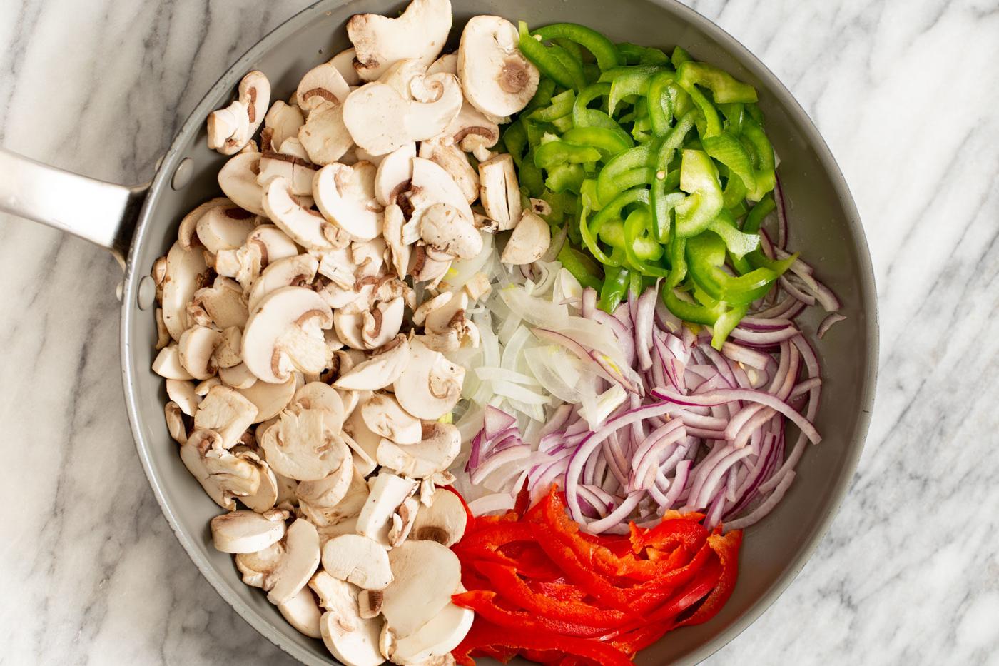 bell peppers, onion and mushrooms in a sauteeing pan