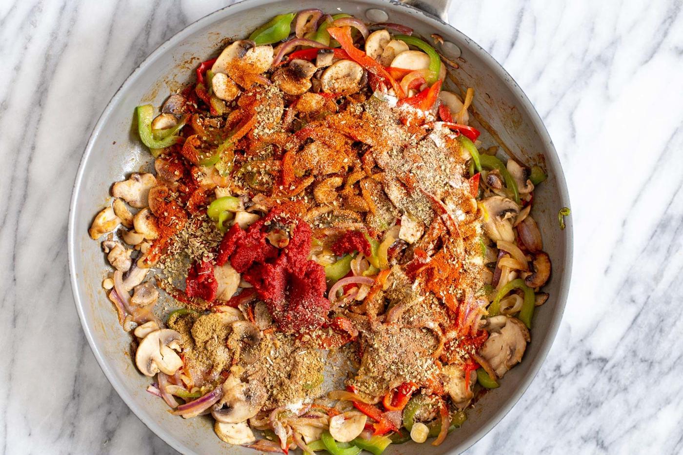 Mexican spices and tomato paste being added to veggies in a pan