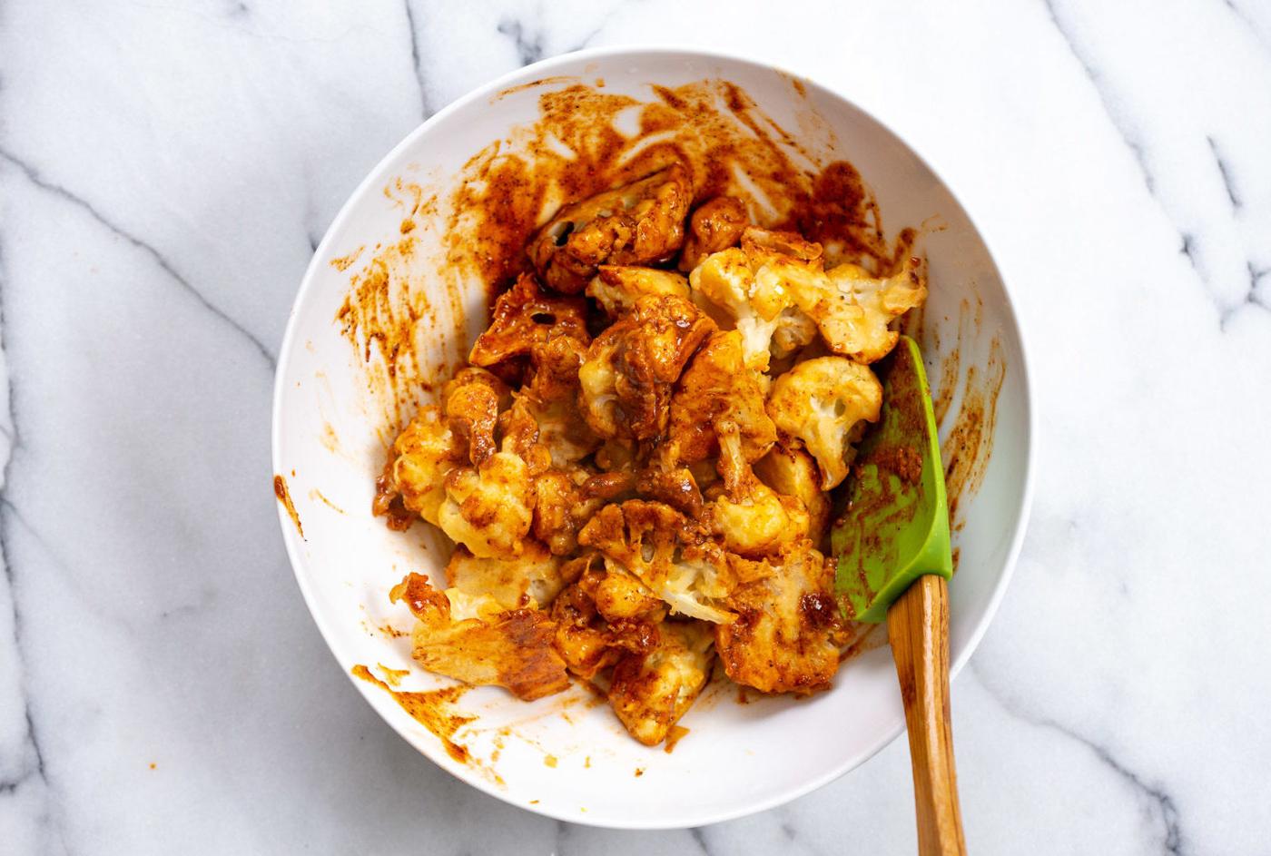 Our Baked Nashville Hot Cauliflower Wings mixed with Nashville hot sauce in a white bowl