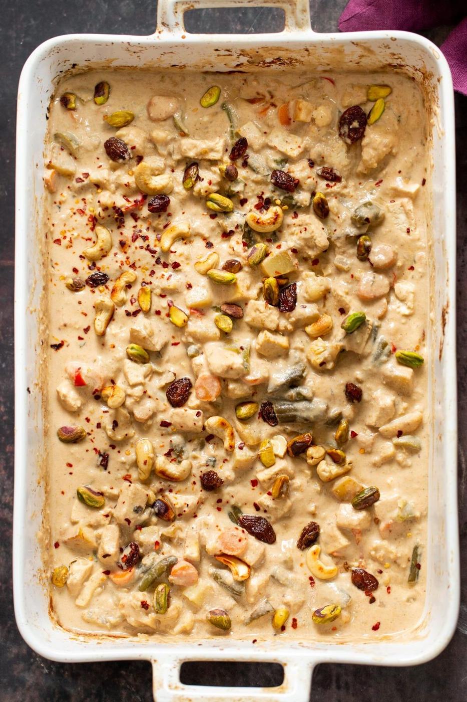 chopped nuts and chili flaked being sprinkled over creamy Navratan Korma
