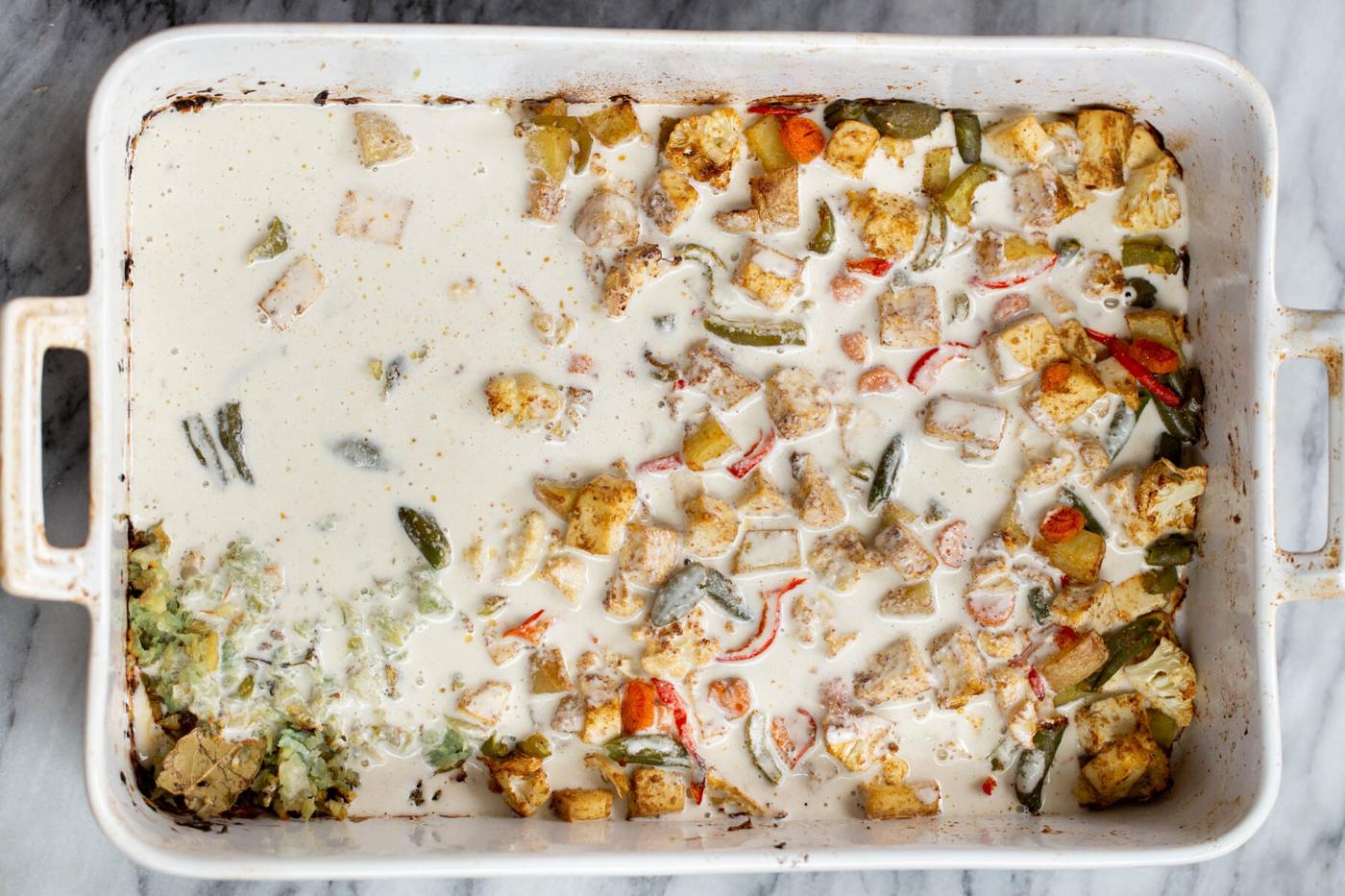 creamy cashew sauce being added to roasted veggies in a casserole dish