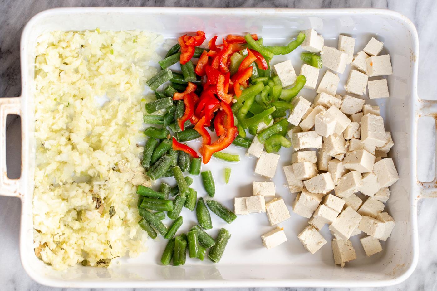 a casserole dish with ginger, garlic and chopped veg as well as tofu in a white casserole dish
