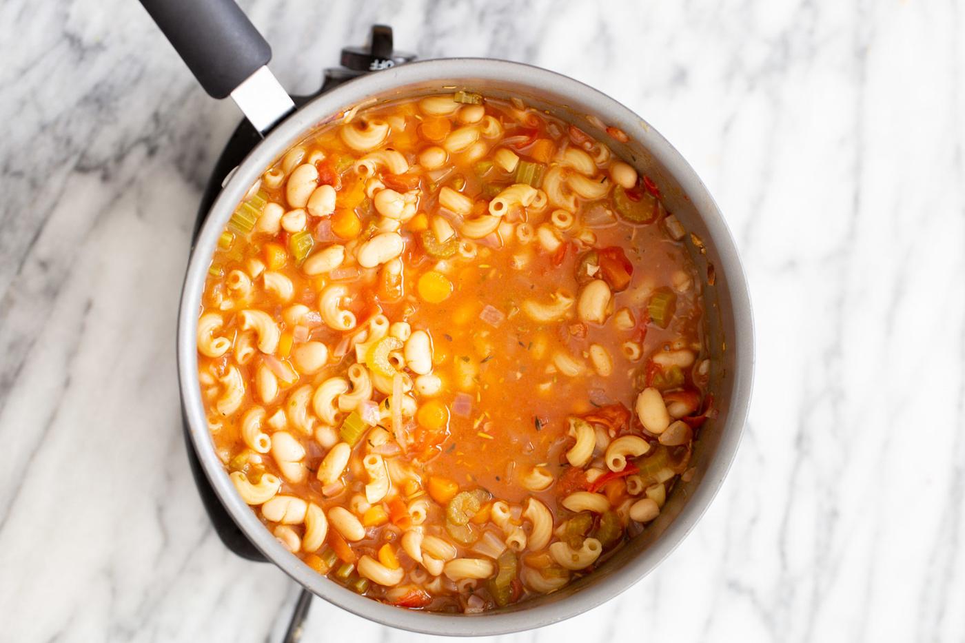 pasta and white beans simmering in tomato broth in a saucepan