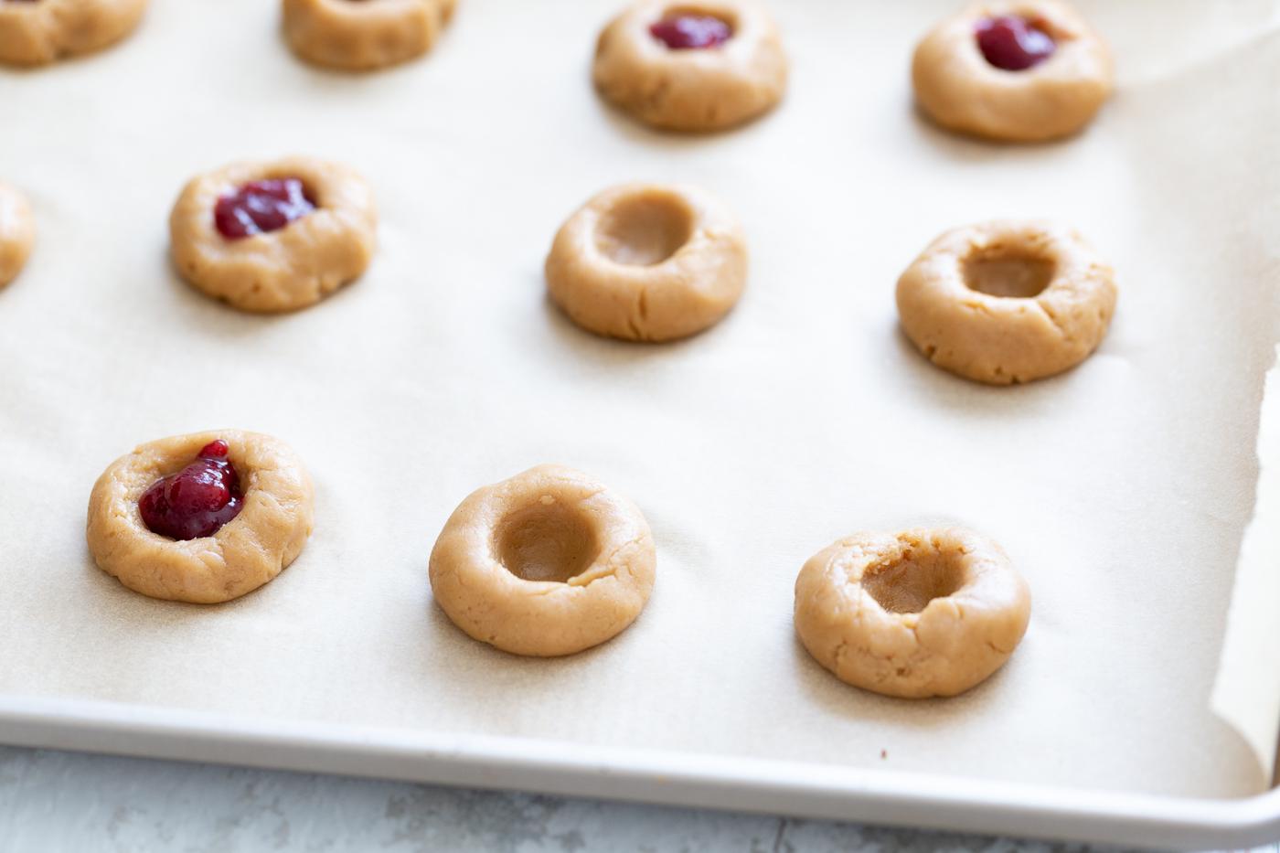 cookie dough balls being indented and filled with jam to make thumbprint cookies