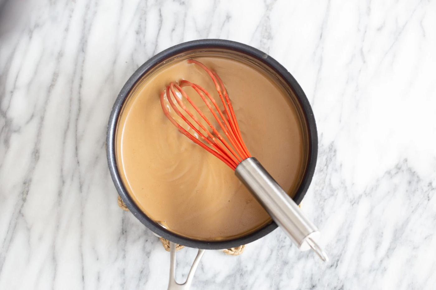base for making peanut butter mousse being whisked in a pot with a red whisk