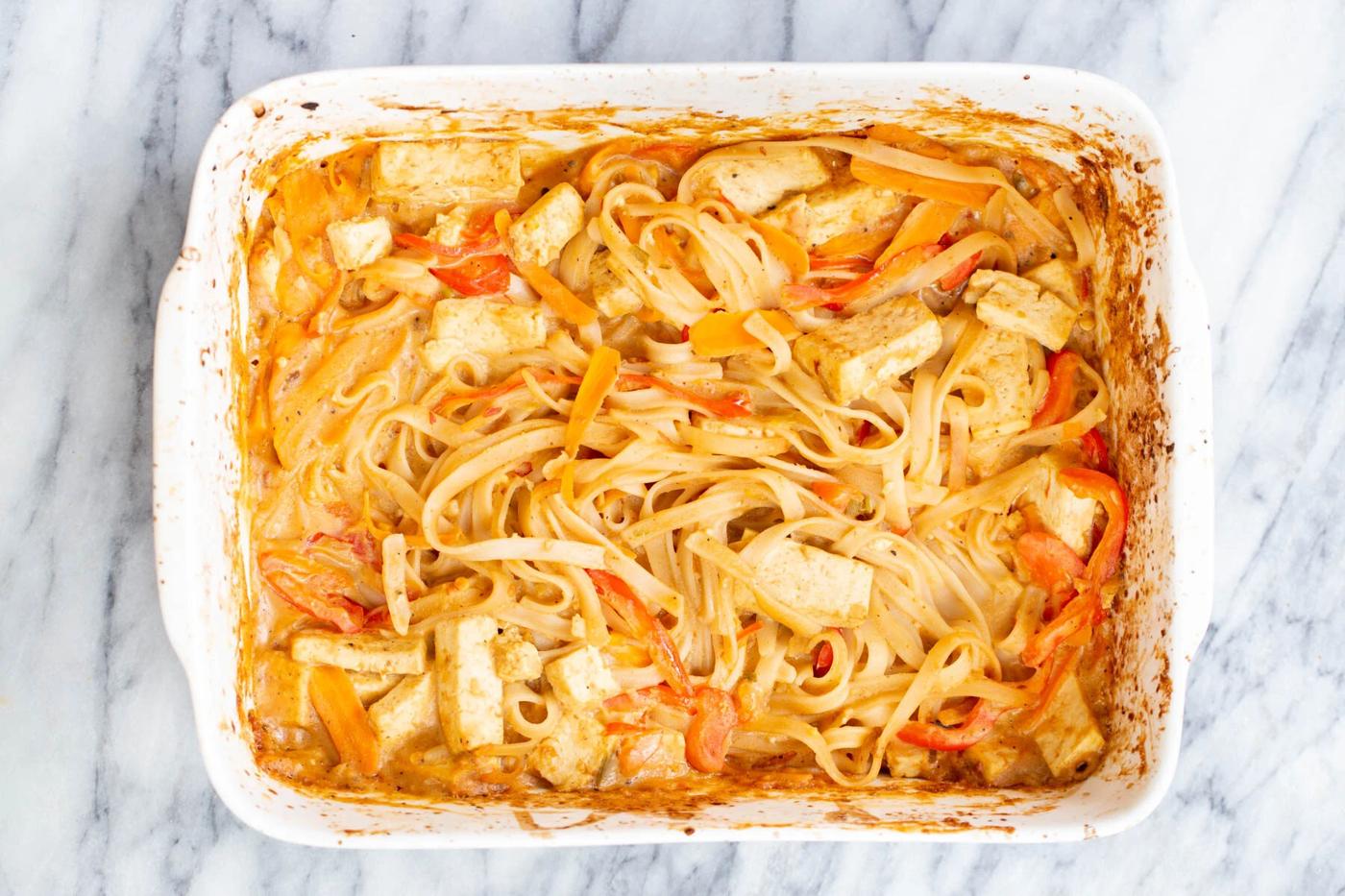 rice noodles being combined with creamy peanut butter sauce in a casserole dish