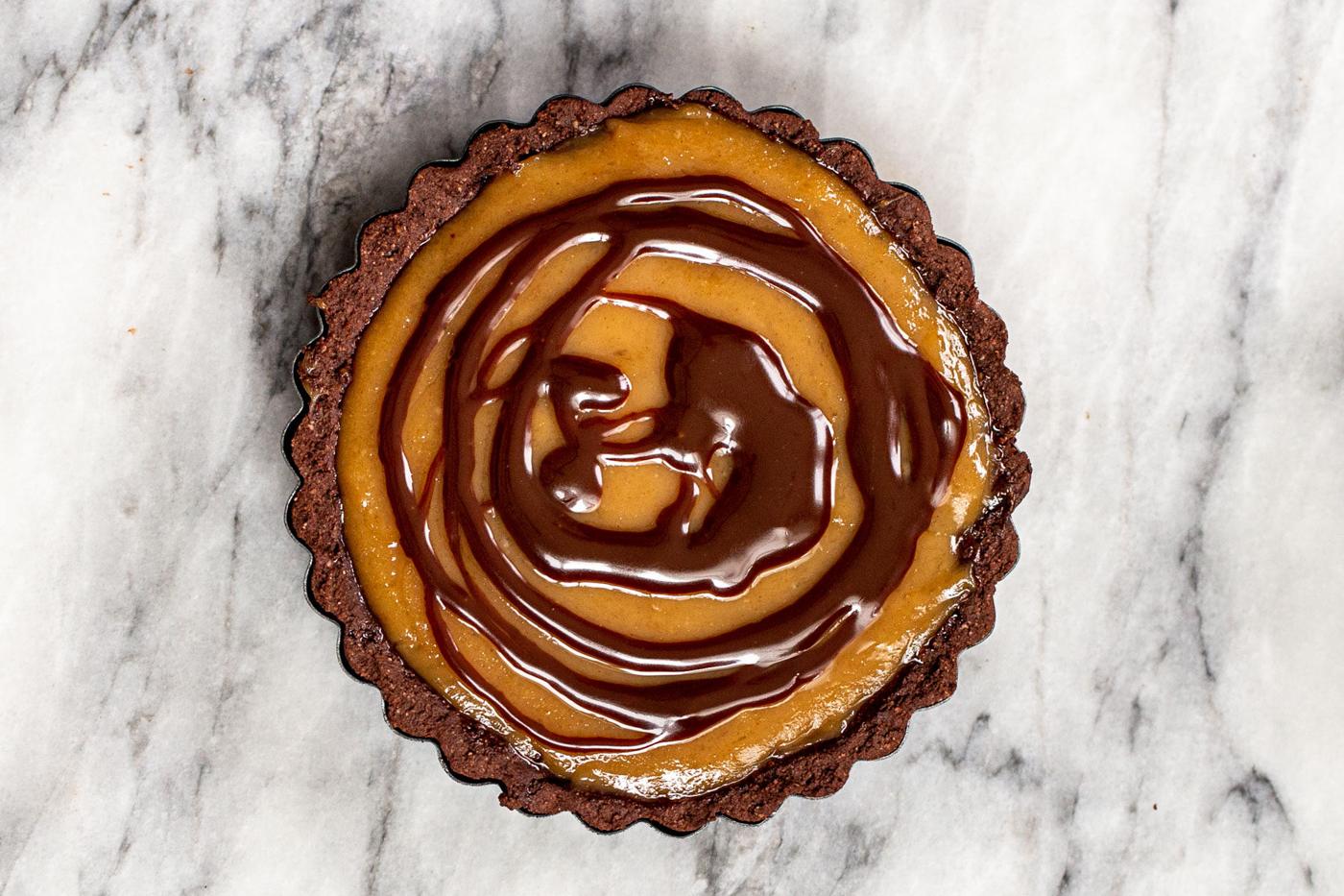 chocolate drizzle being spread over peanut butter filling in a tartshell
