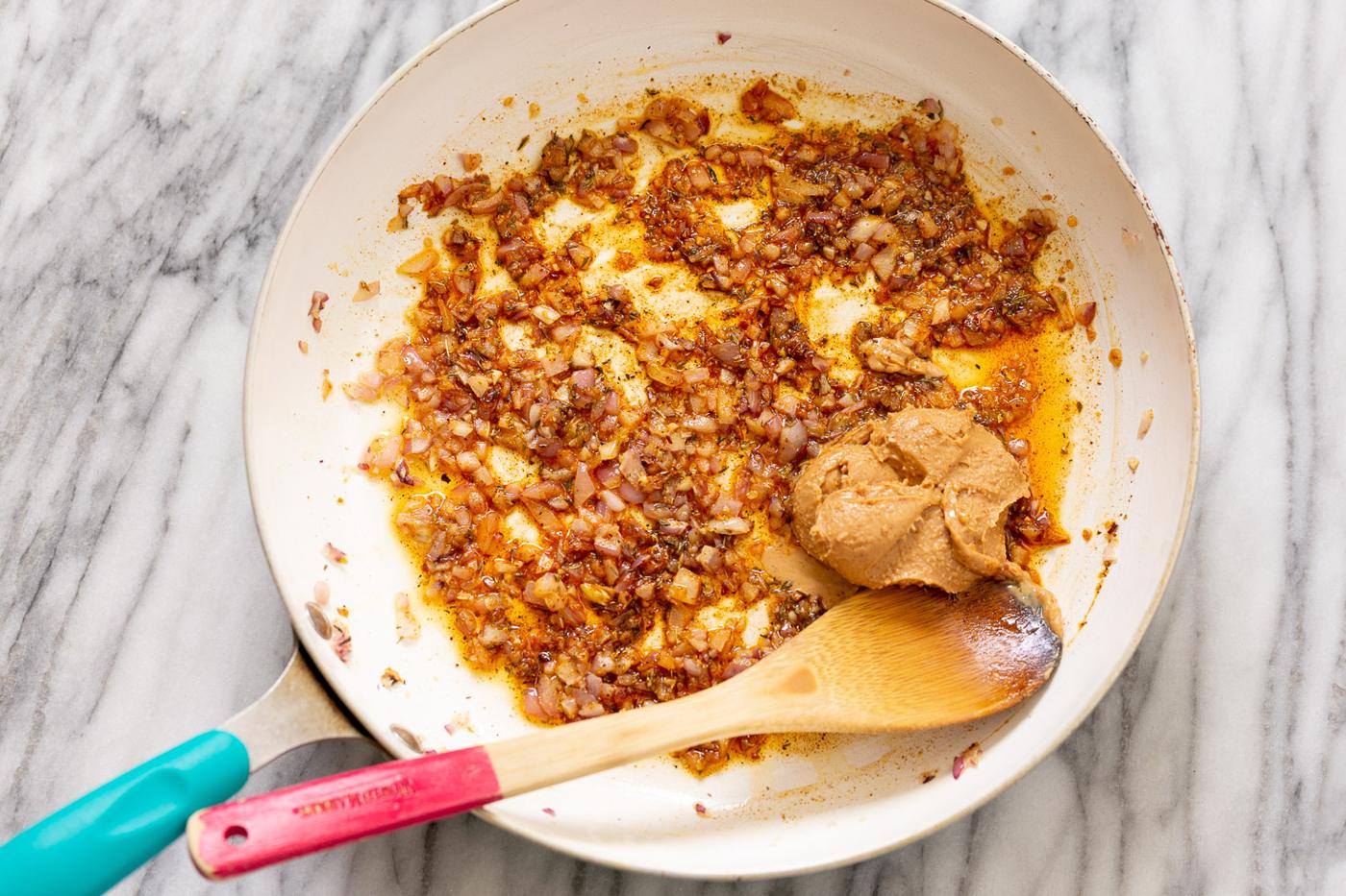 minced onions being sauteed in a frying pan with spices and peanut butter for making African peanut stew